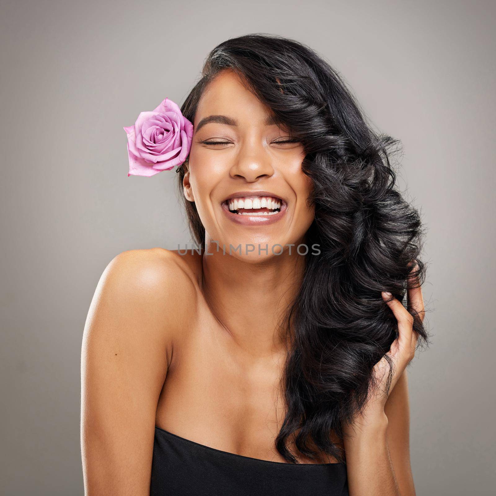 Maybe its her hair or maybe its her personality. Shot of a beautiful young woman posing with a flower in her hair. by YuriArcurs