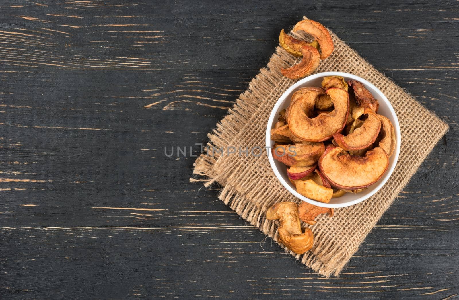 Bowl of dry Apple slices on sackcloth and wooden background, top view