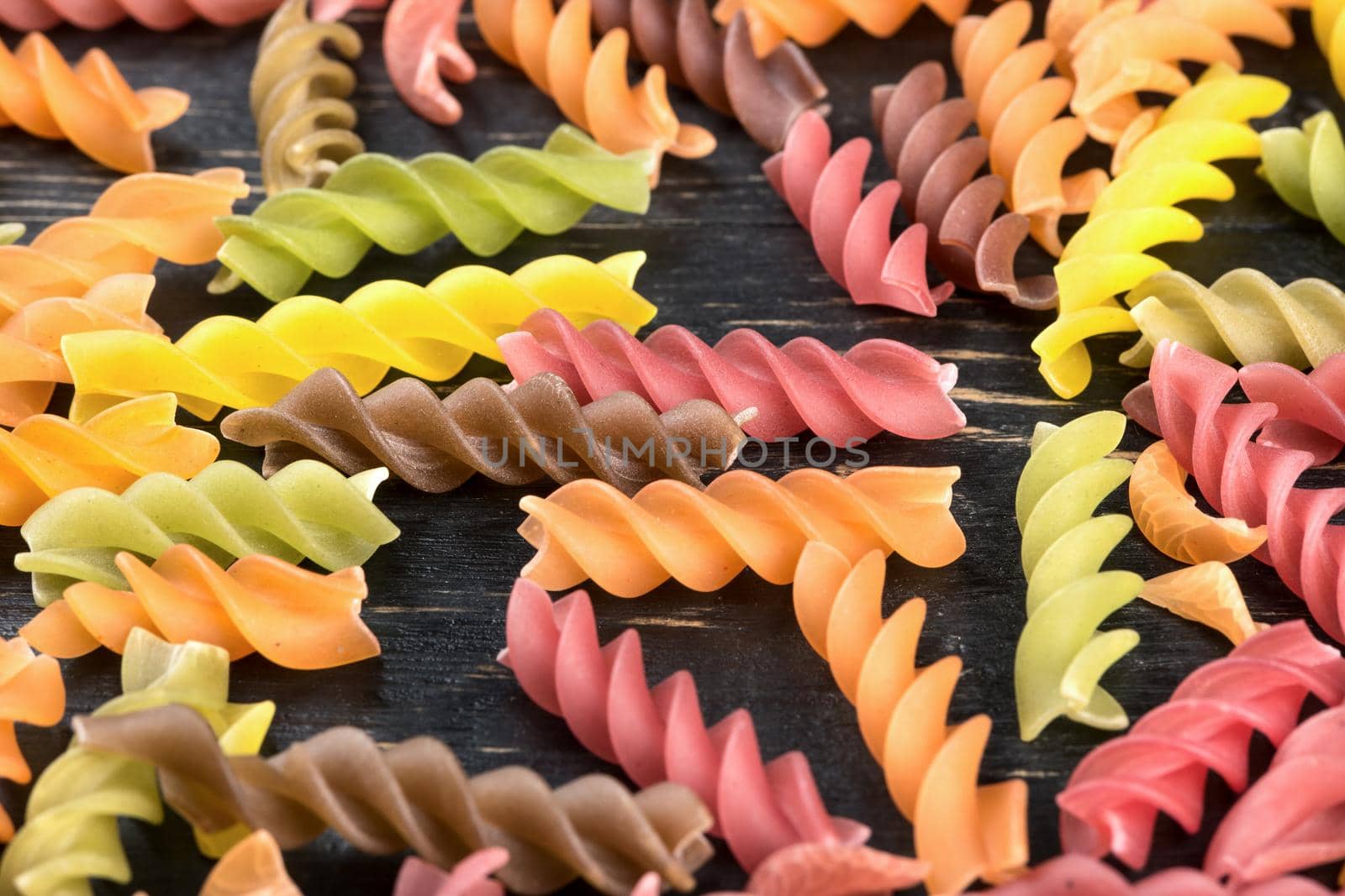 Scattered multi-colored raw pasta fusilli on wooden background