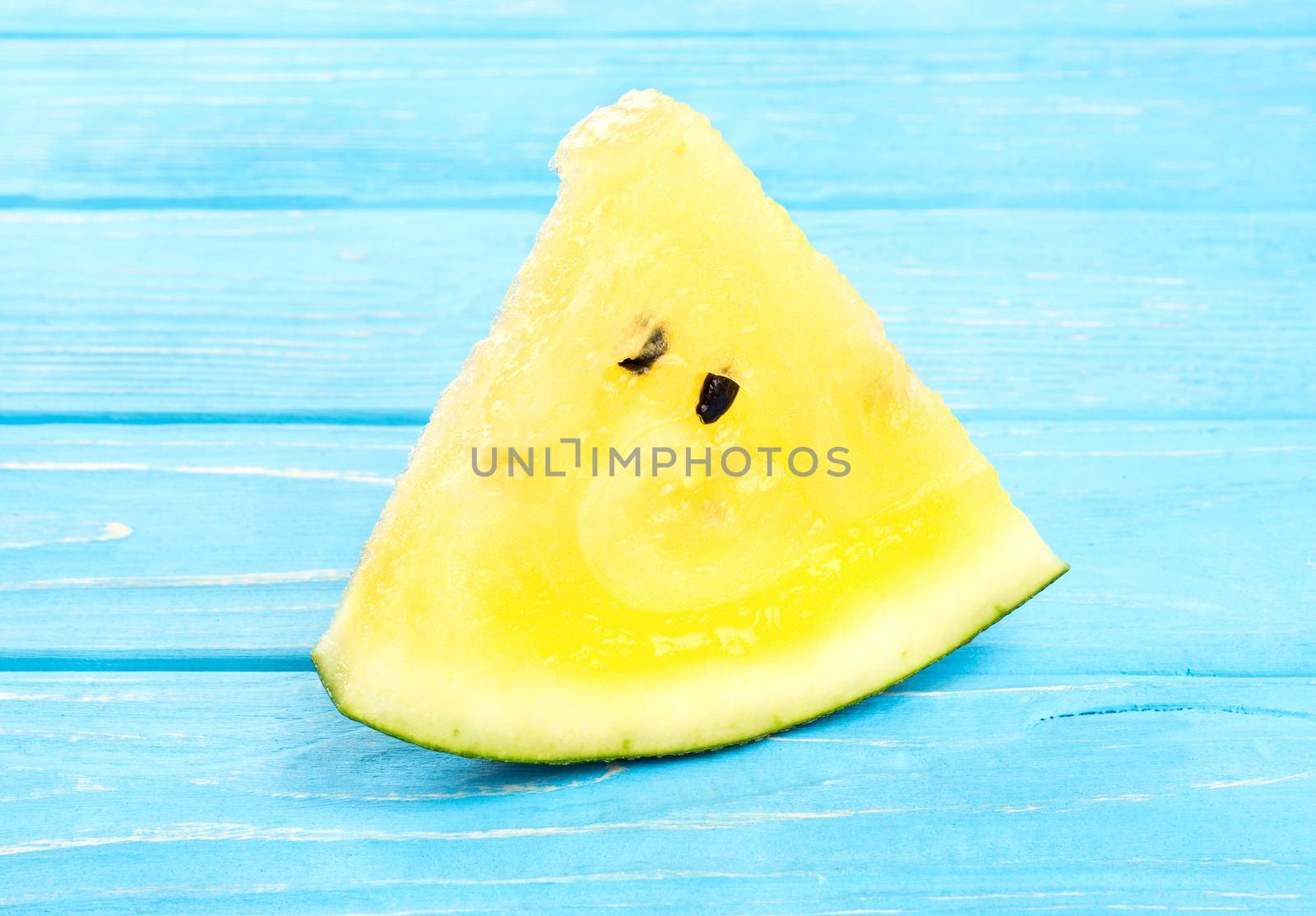 Triangular slice of yellow watermelon on a blue table