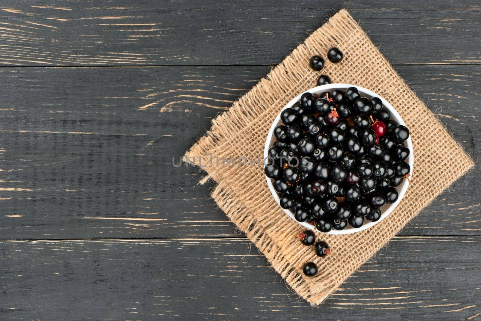 Bowl of bird cherries on sackcloth and empty wooden background