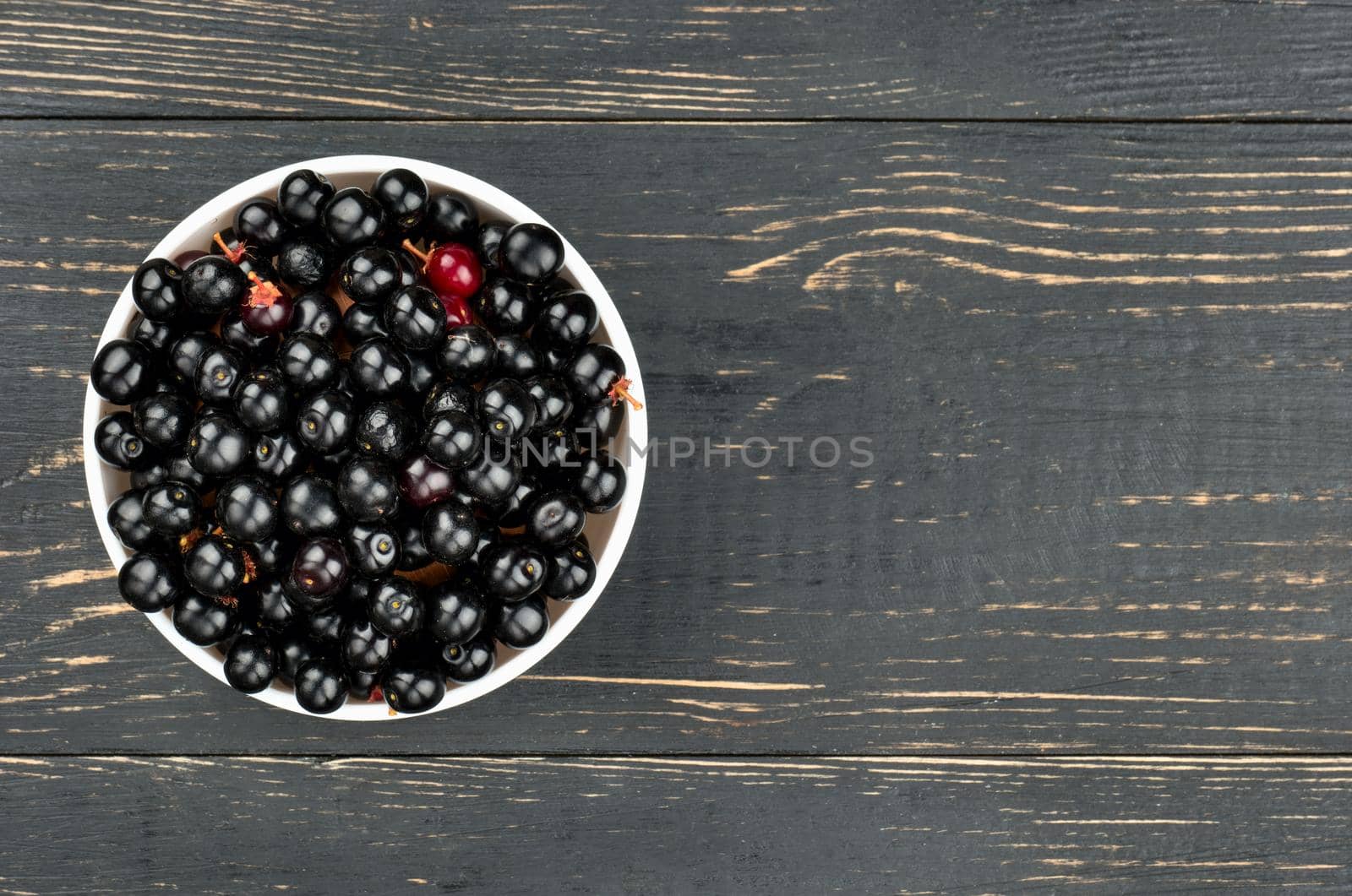 White bowl of bird cherries on an empty wooden background, top view