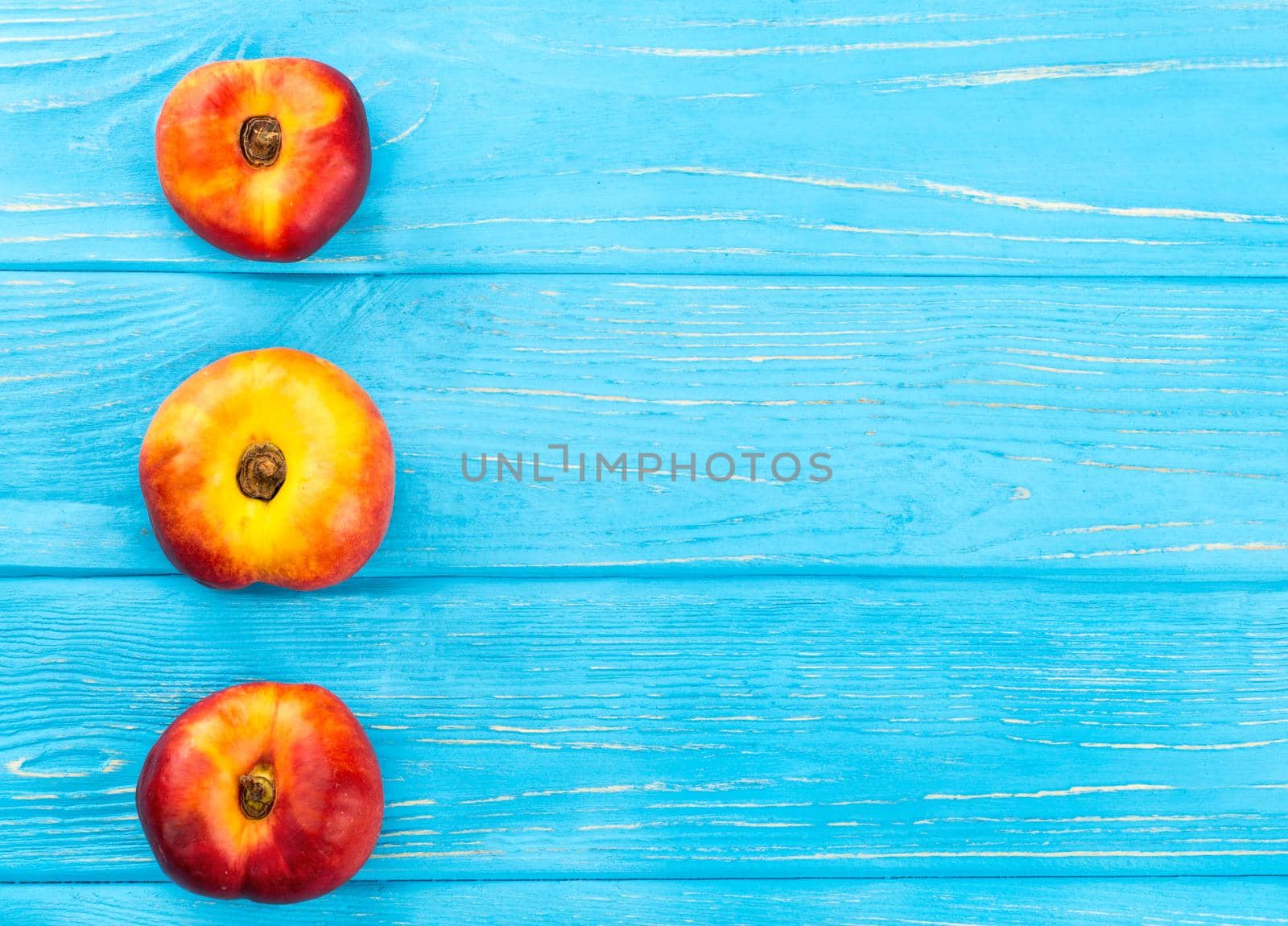 Three ripe flat peaches on a empty wooden background, top view