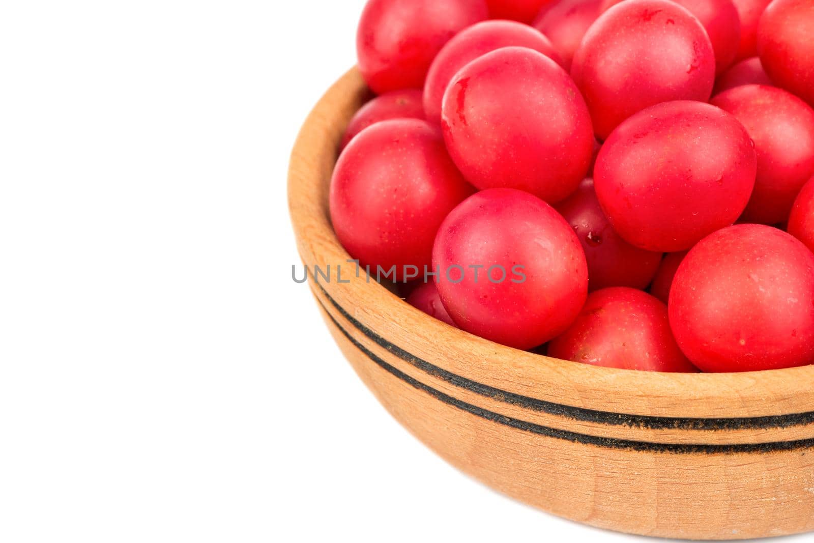Part of a wooden bowl filled with red cherry plums on a white background