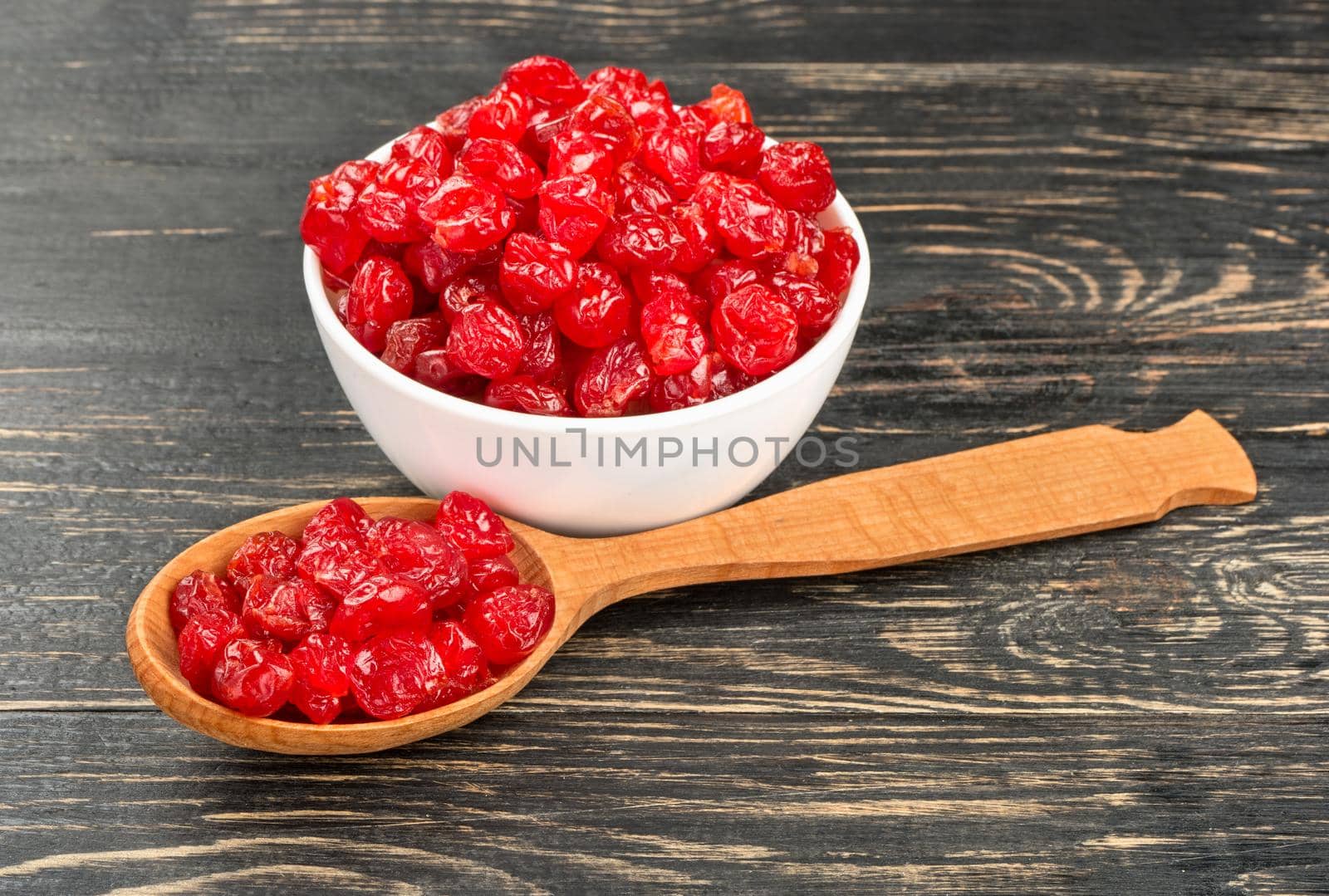Delicious dried cherries in a spoon and bowl on wooden background