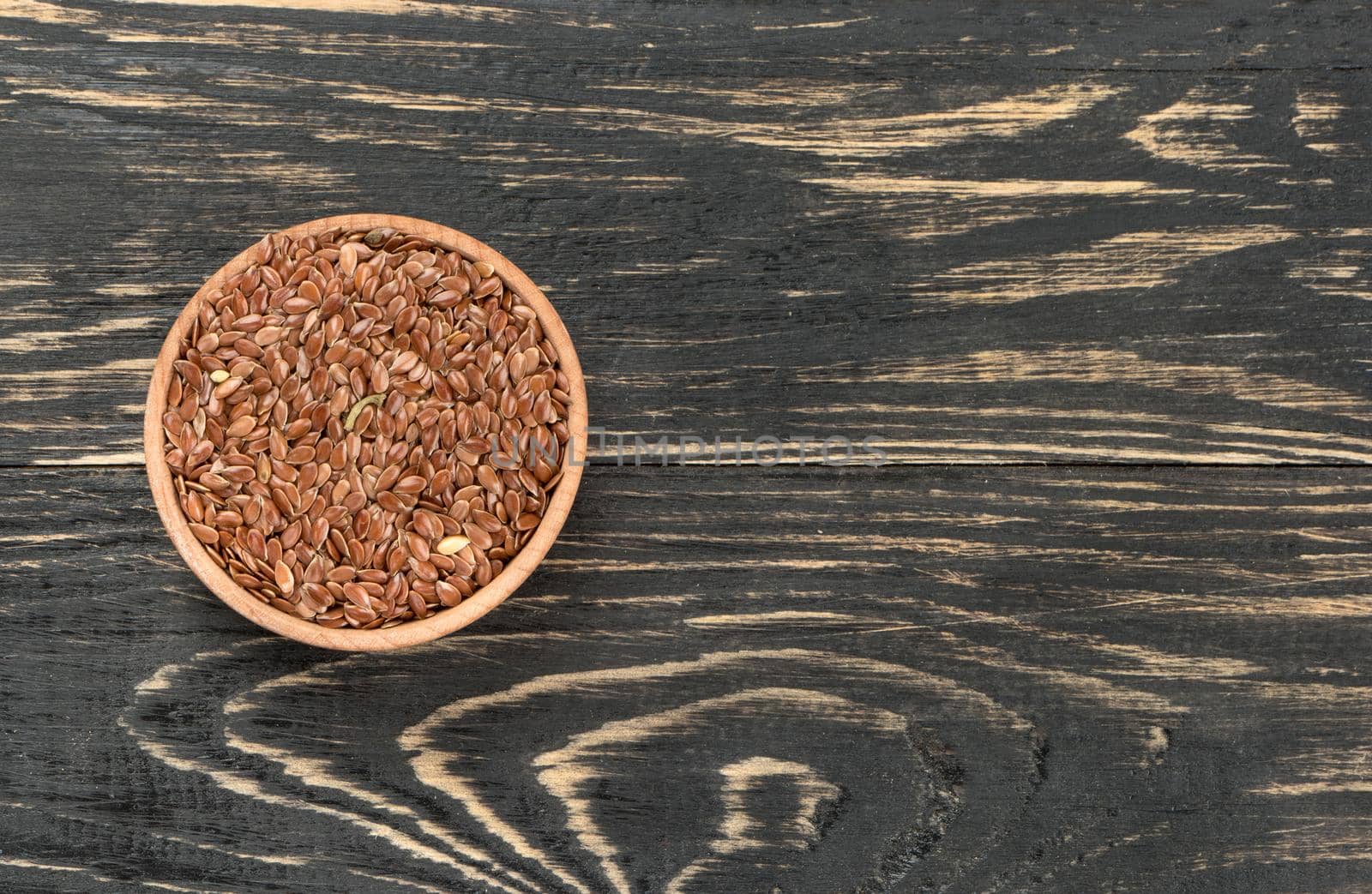 Flax seeds in the empty bowl on wooden background, top view