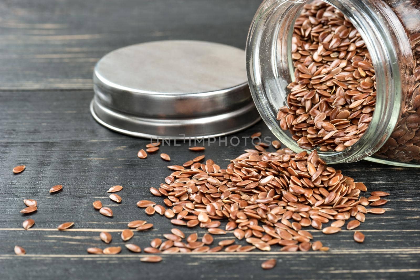 Flax seeds are scattered from jar closeup on wooden background