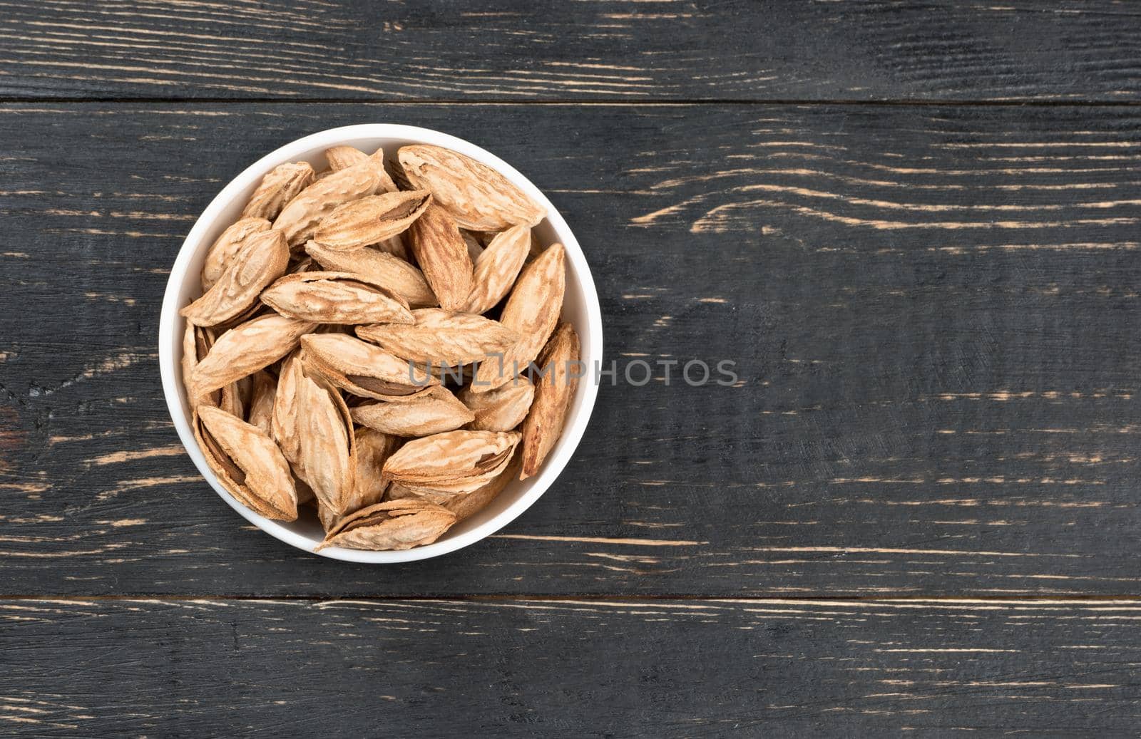 Ceramic bowl filled with Uzbek inshell almonds on wooden background