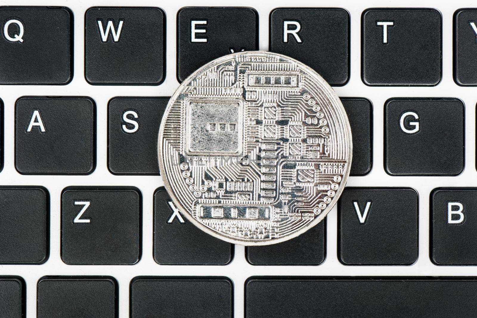 Back side of a silver coin bitcoin on a close-up keyboard top view