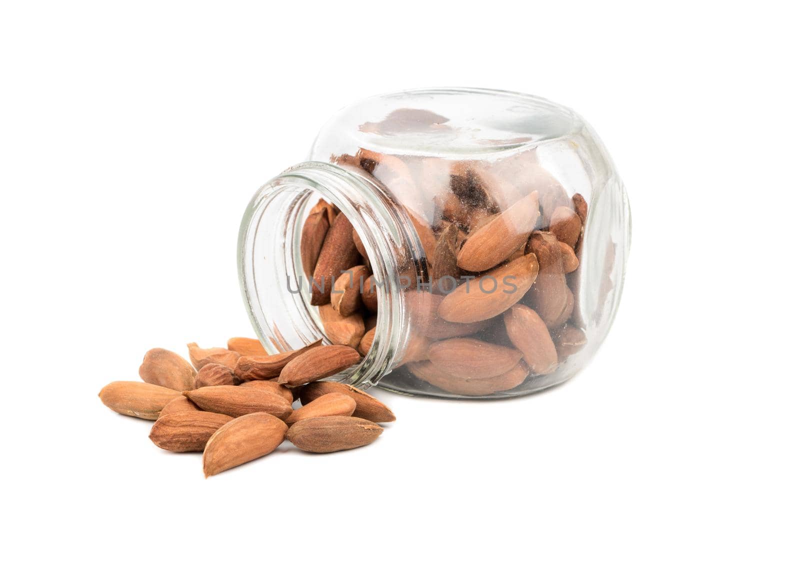 Scattered Uzbek almonds from a glass jar on a white background
