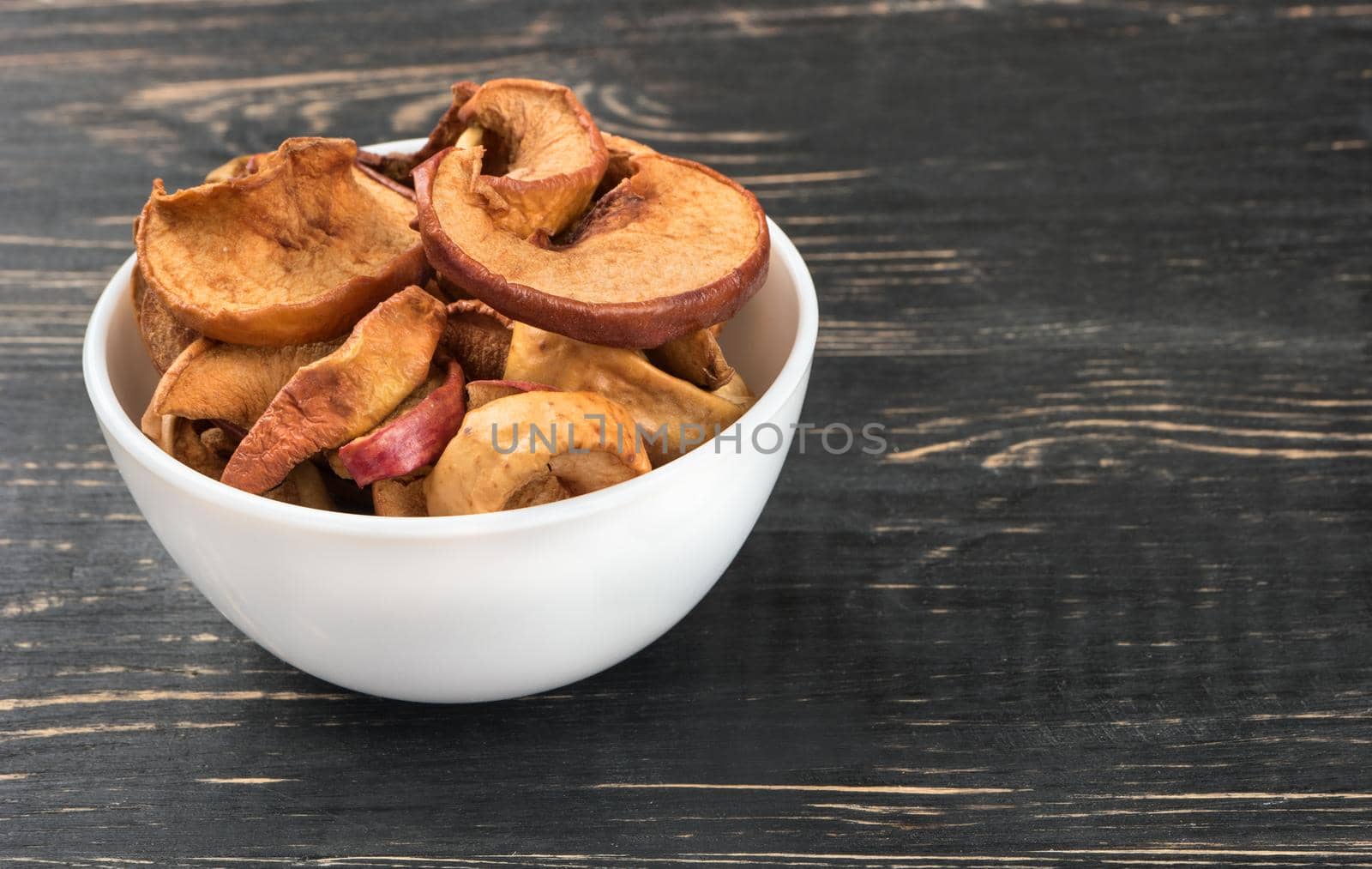 Dry apple slices in ceramic bowl on wooden background