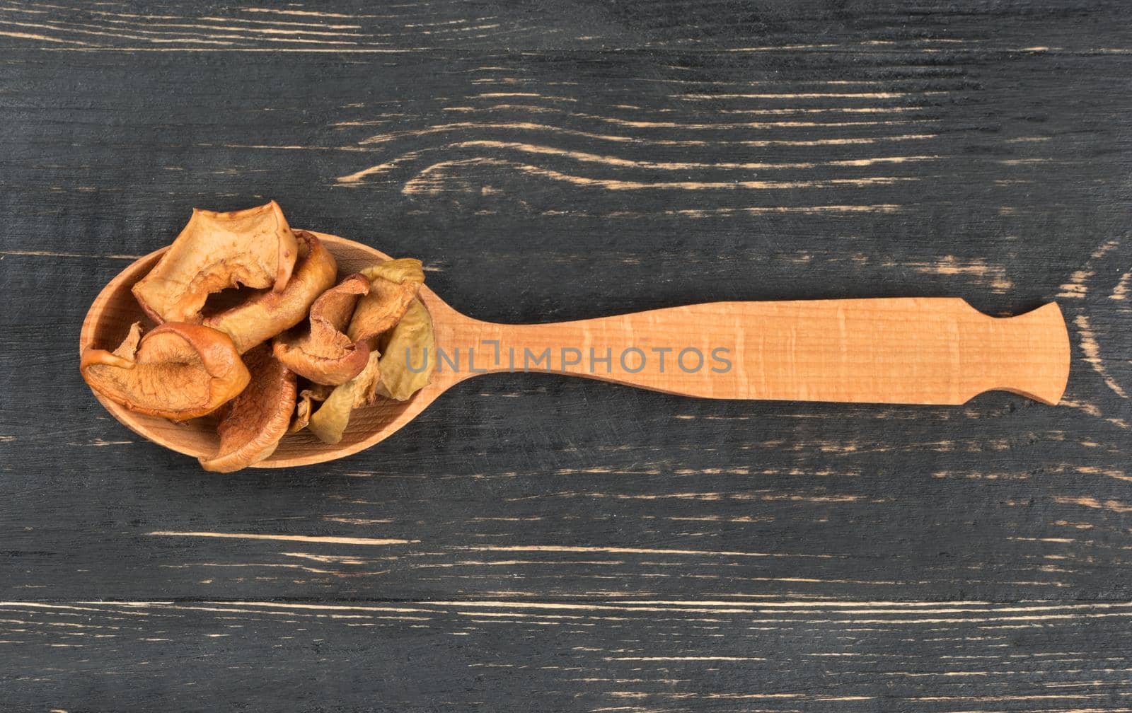 Slices of dried apples in a spoon on wooden background top view