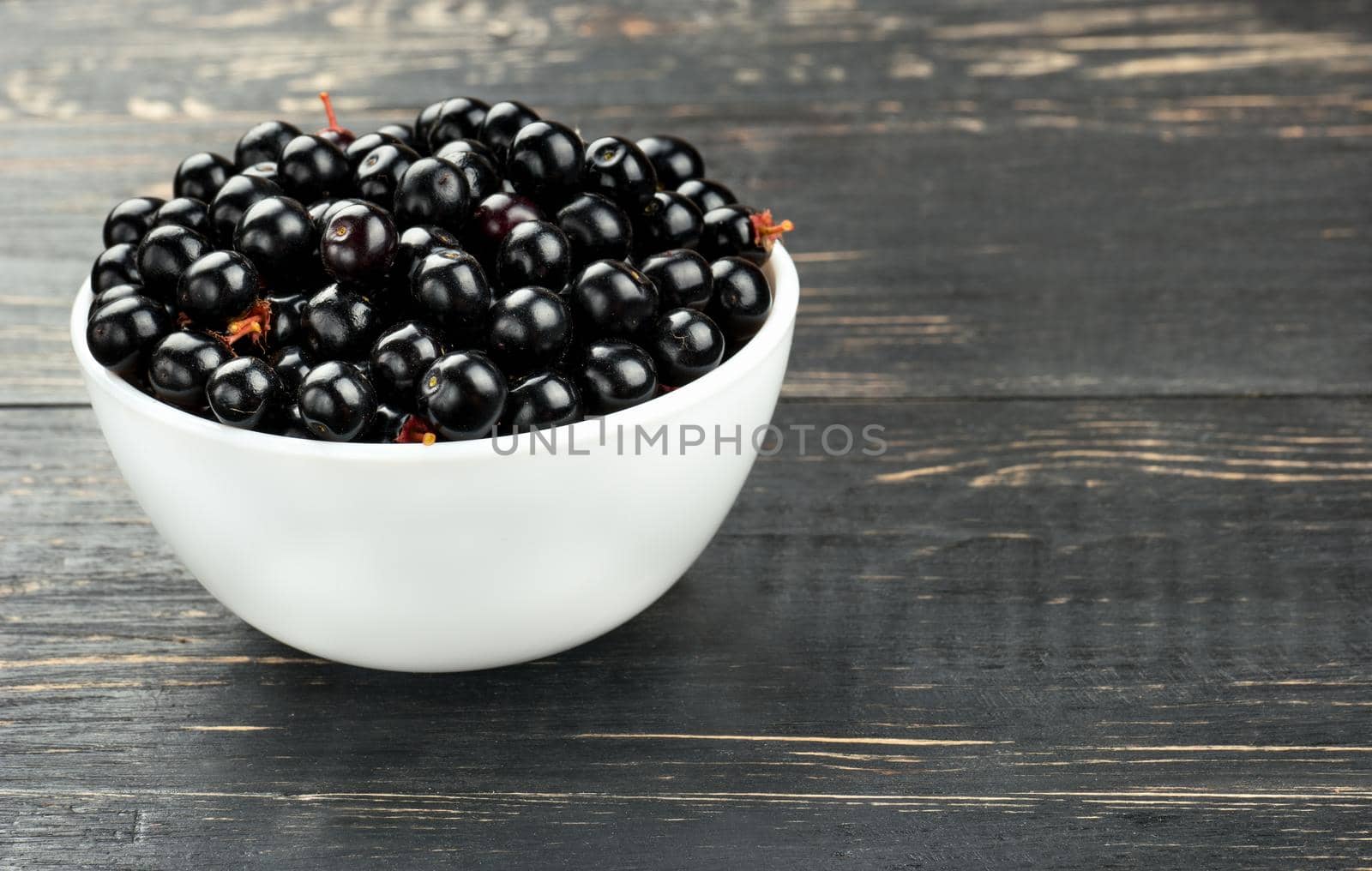 White bowl of bird cherries on a dark table closeup