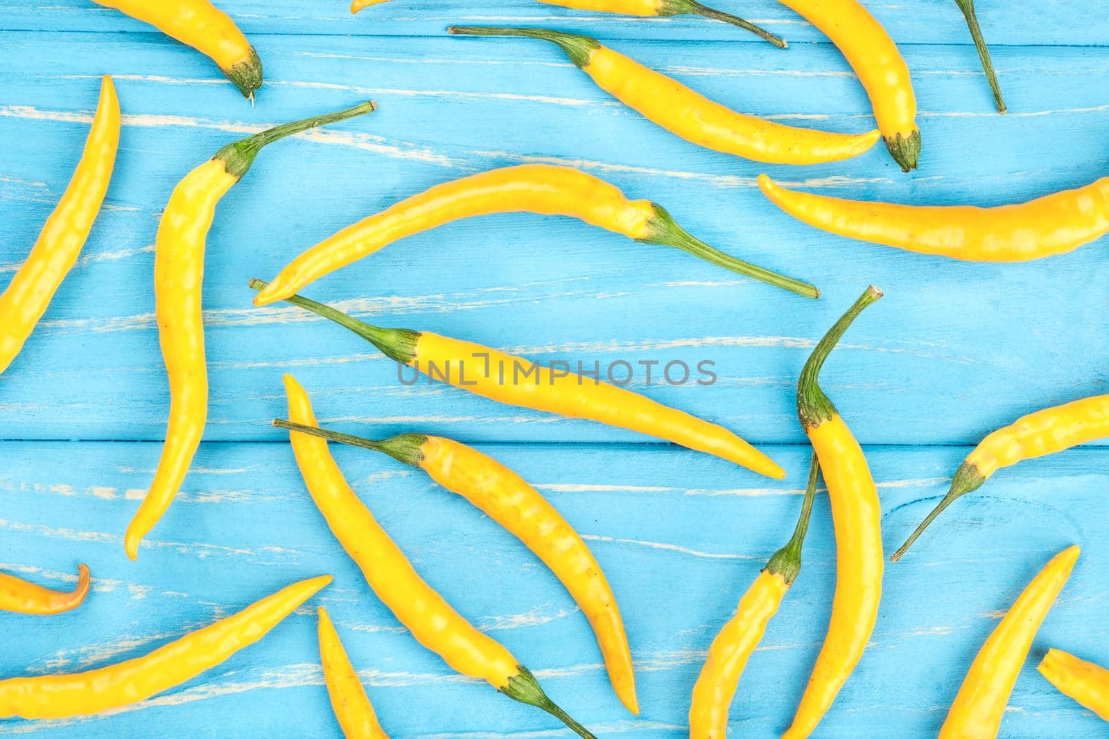 Scattered yellow chili peppers on a wooden background, top view
