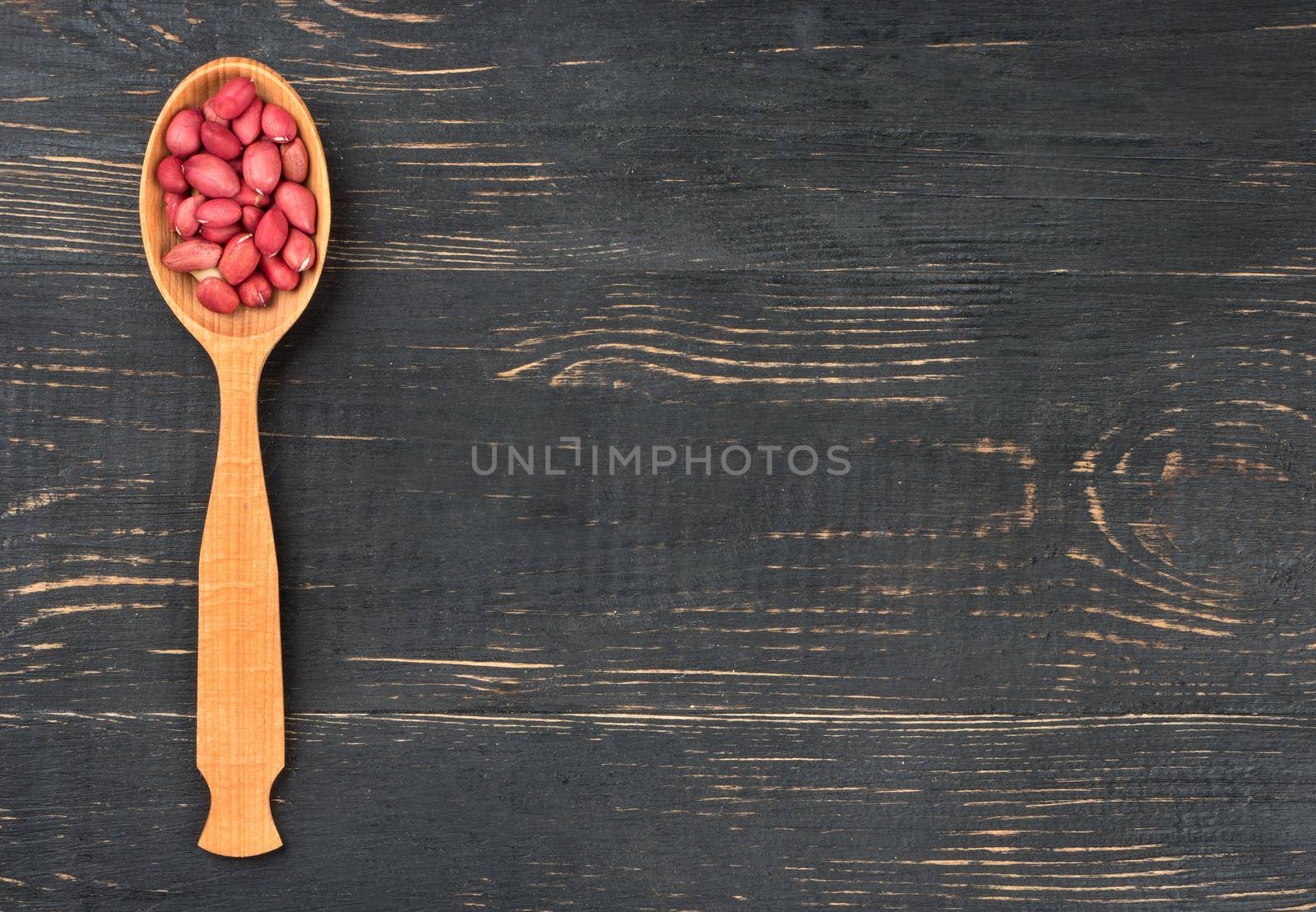 Kernel dry peanut in the empty spoon on wooden background, top view