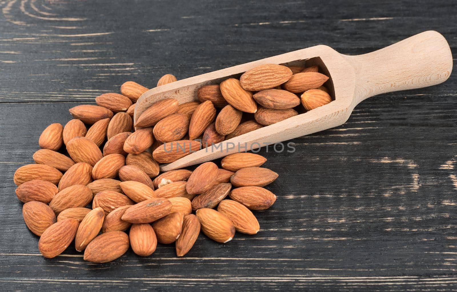 Scattered almond nuts with a scoop on dark wooden background