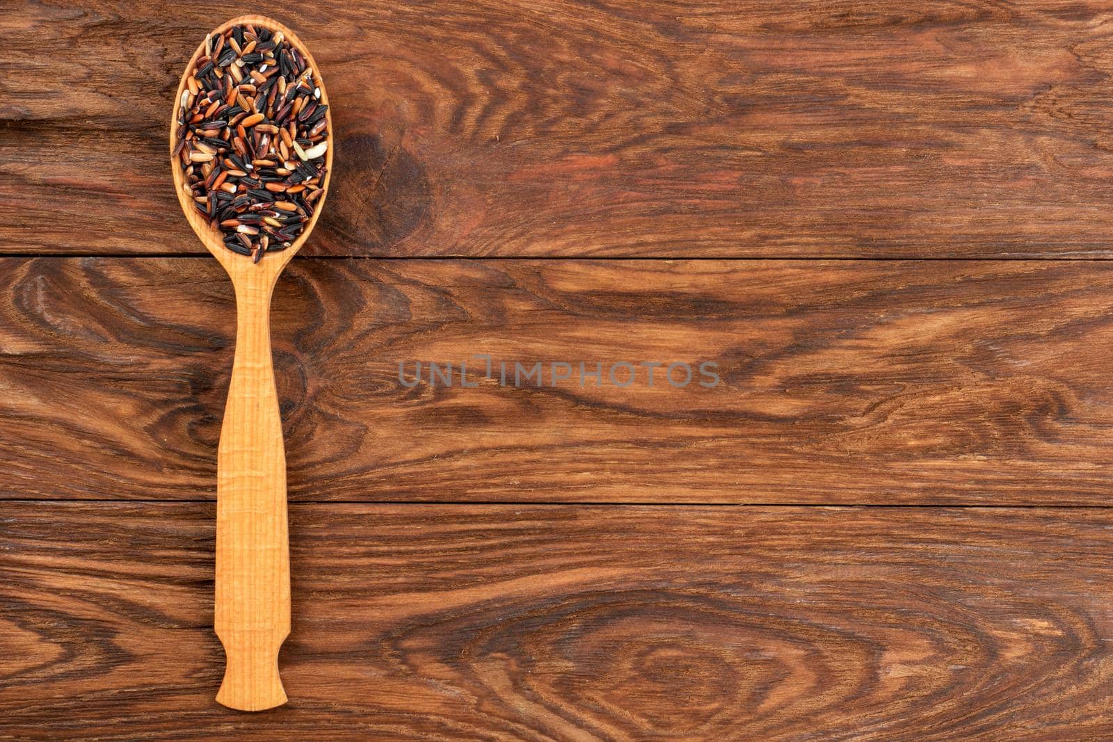 Wild rice in spoon on empty wooden background