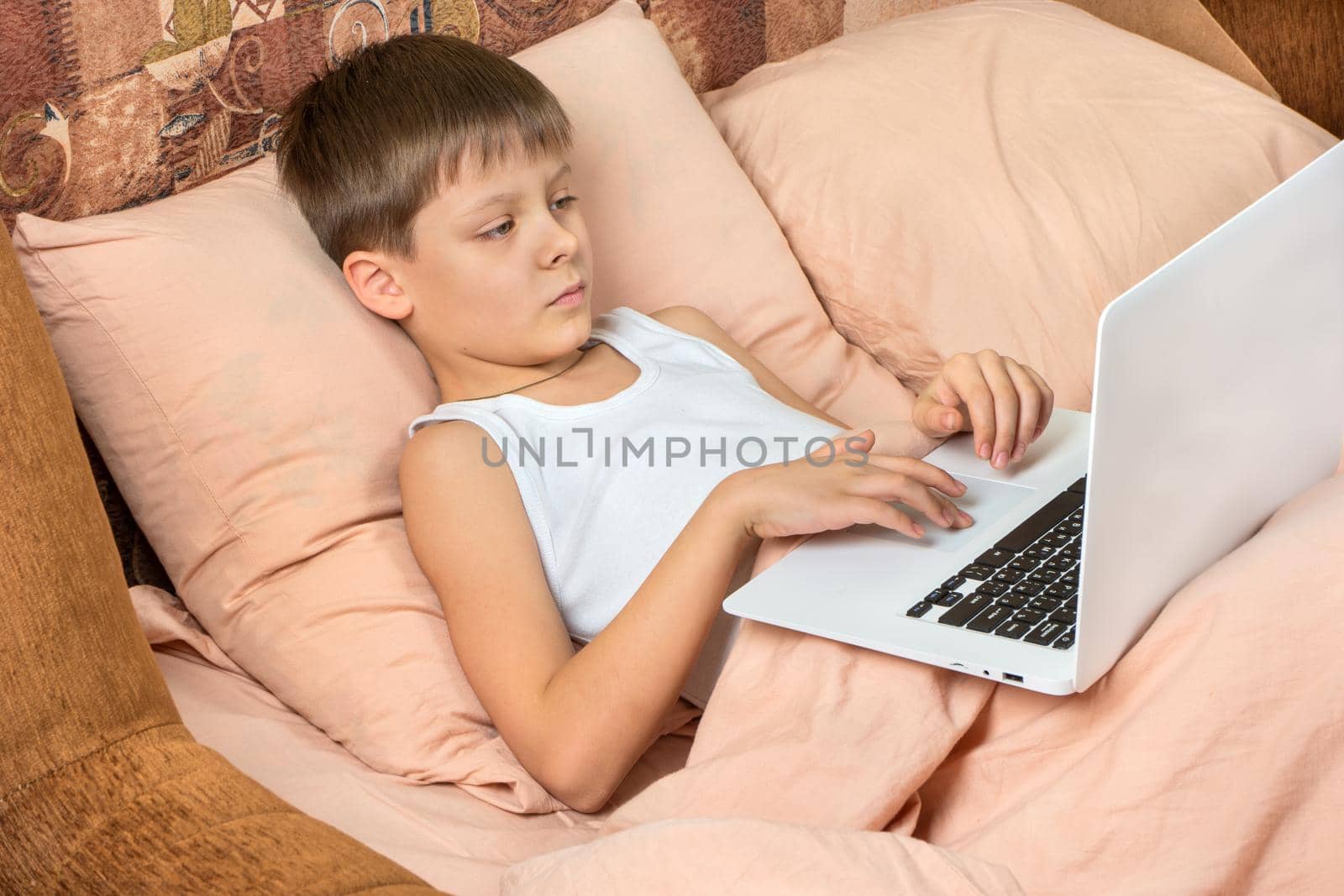 Young boy plays games on a laptop in bed