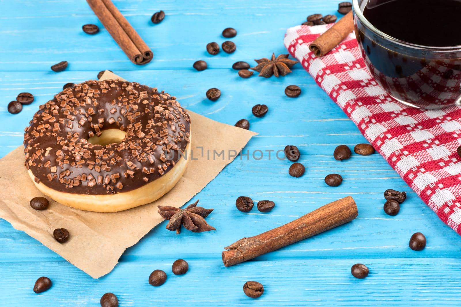 Delicious chocolate donut with a cup of coffee and beans on a blue wooden background