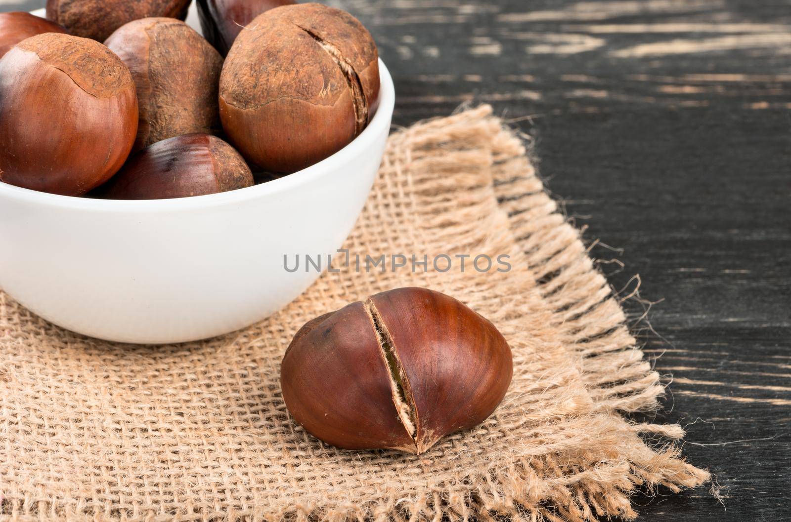 Roasted chestnuts in a white bowl on burlap closeup