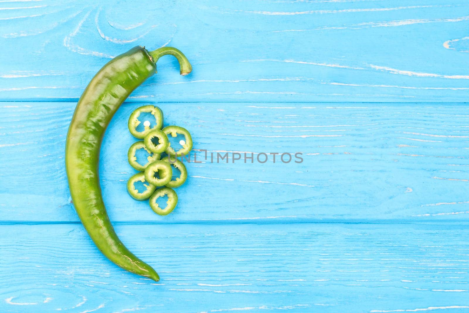 Fresh green chili pepper with slices on a blue wooden background, top view
