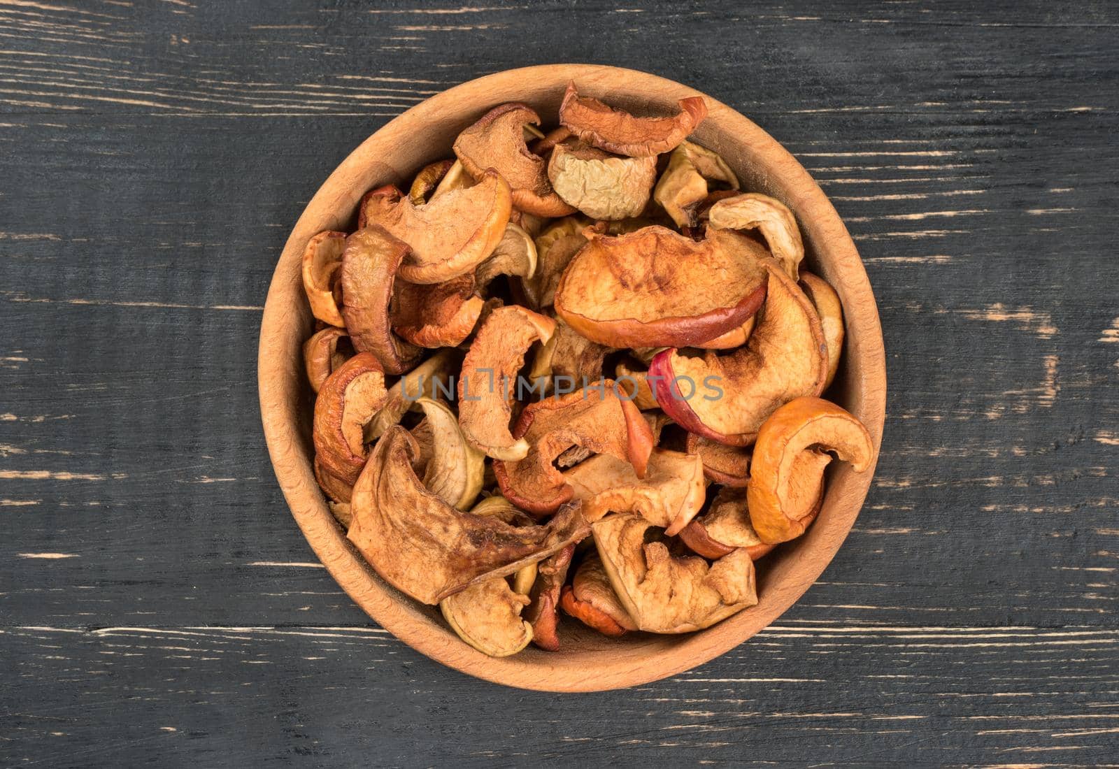 Bowl of dry slices of apples on wooden background, top view