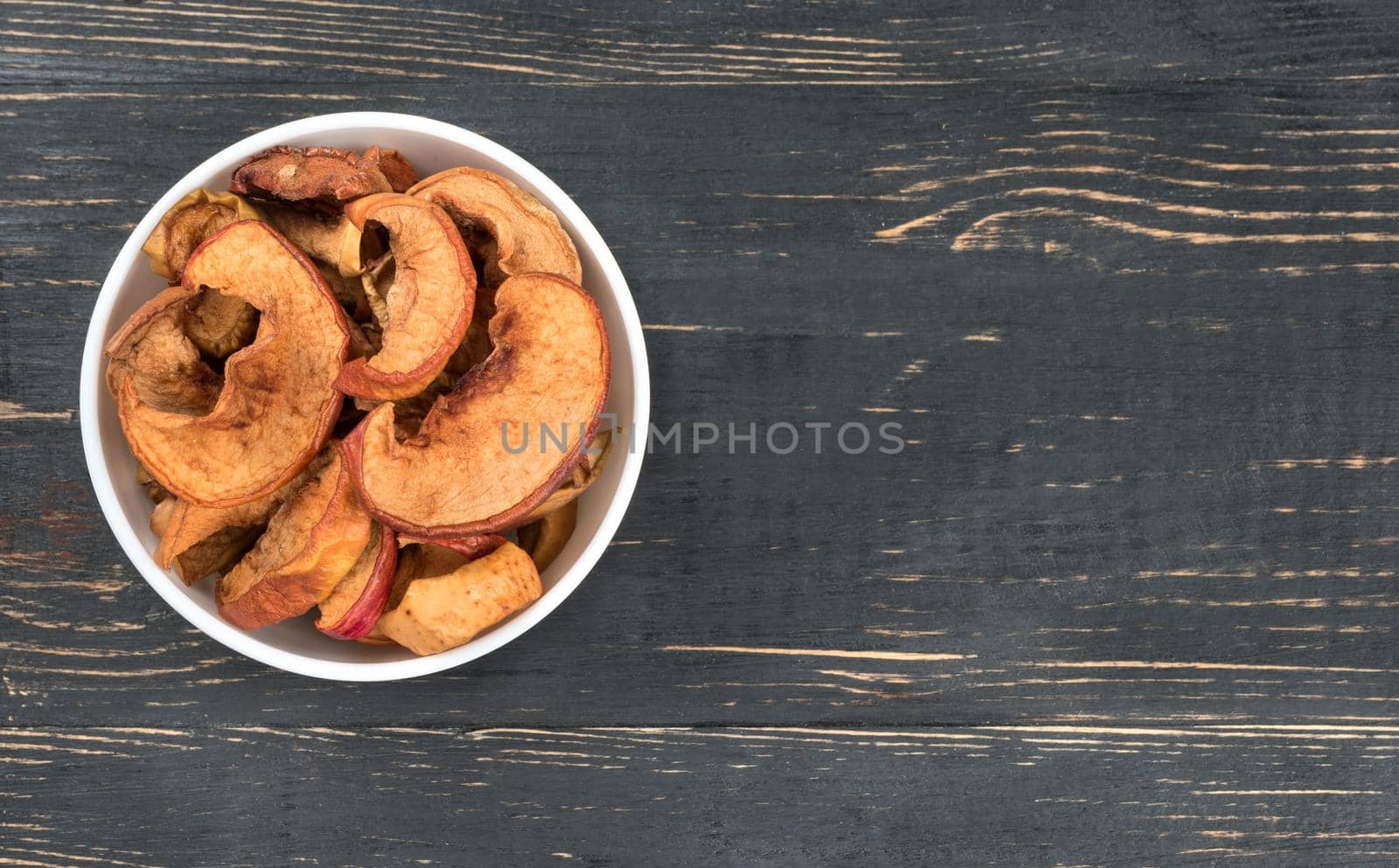 Dry apple slices in a white bowl on a light wooden background