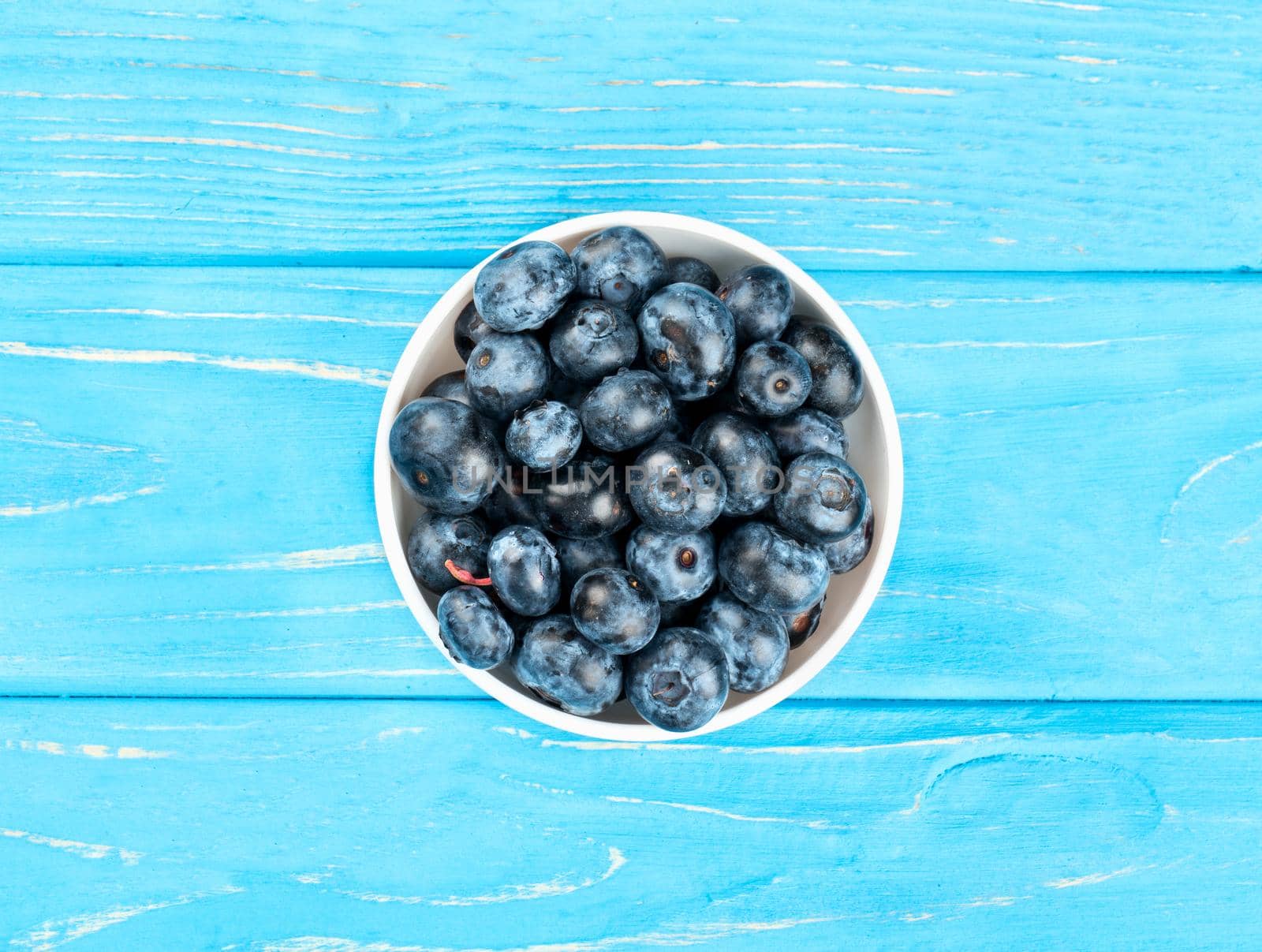 Ceramic bowl full of fresh blueberries on a wooden background, top view
