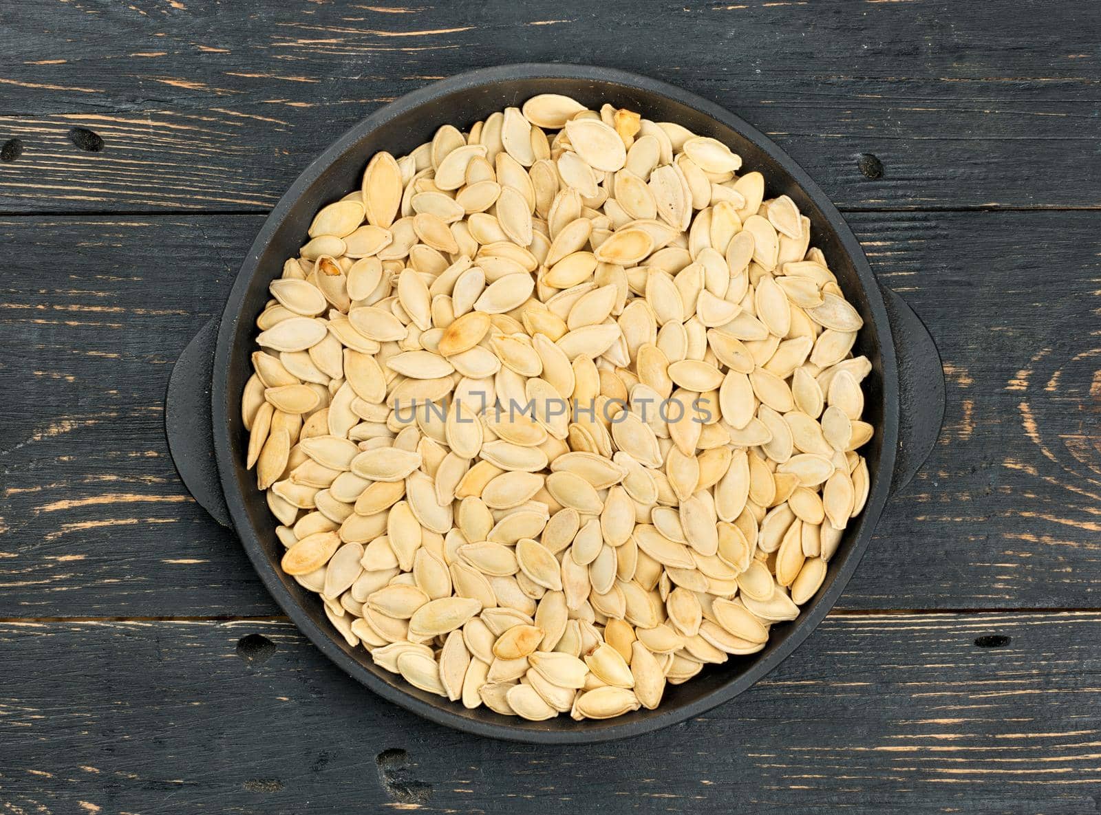 Pumpkin seeds in a shell on a frying pan and table, top view