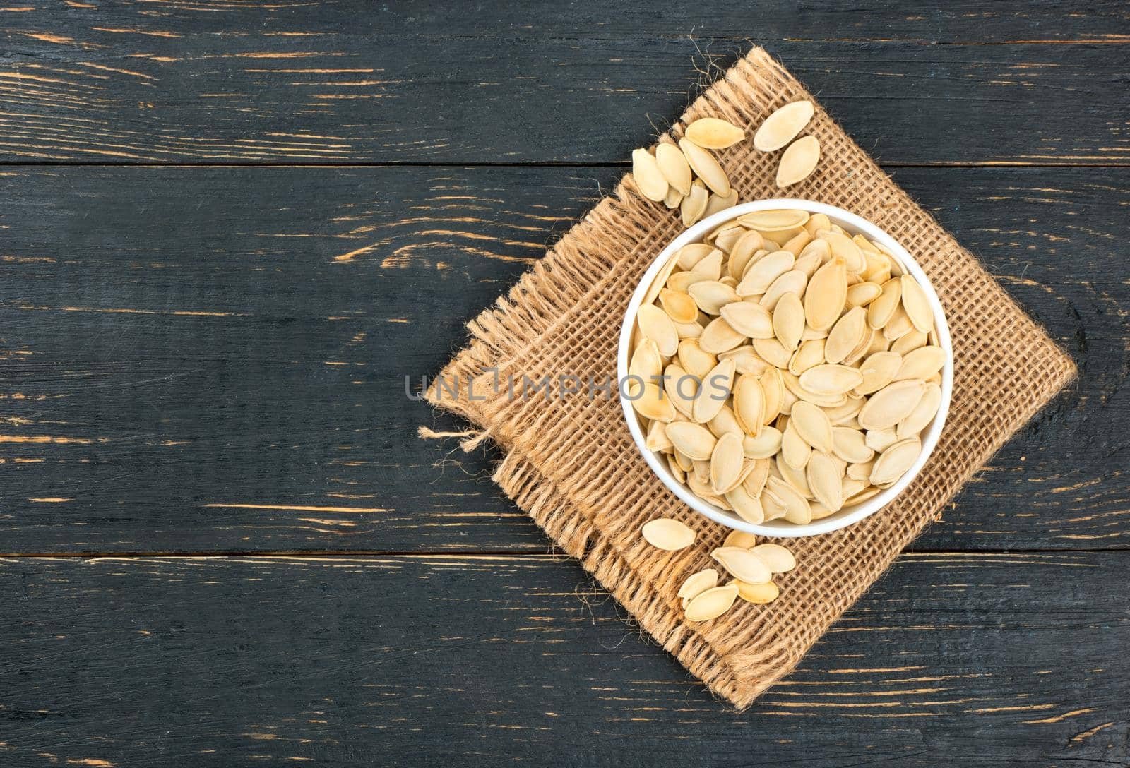 Bowl with pumpkin seeds on burlap and empty wooden background
