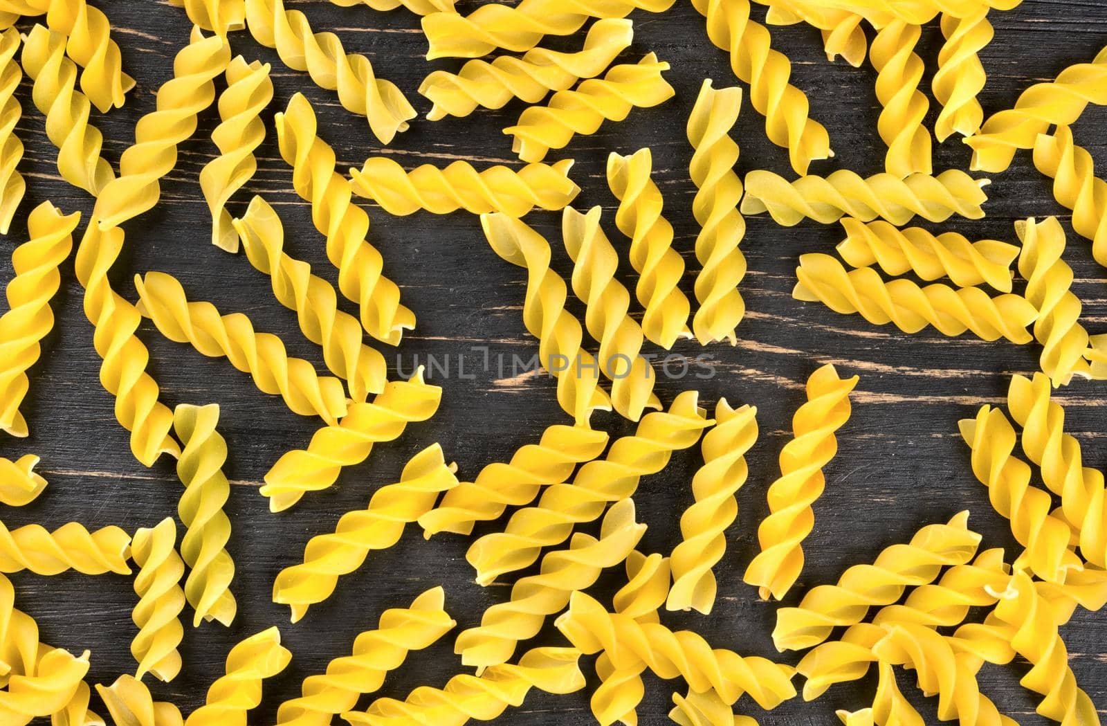 Scatter pasta fusilli wooden background, top view