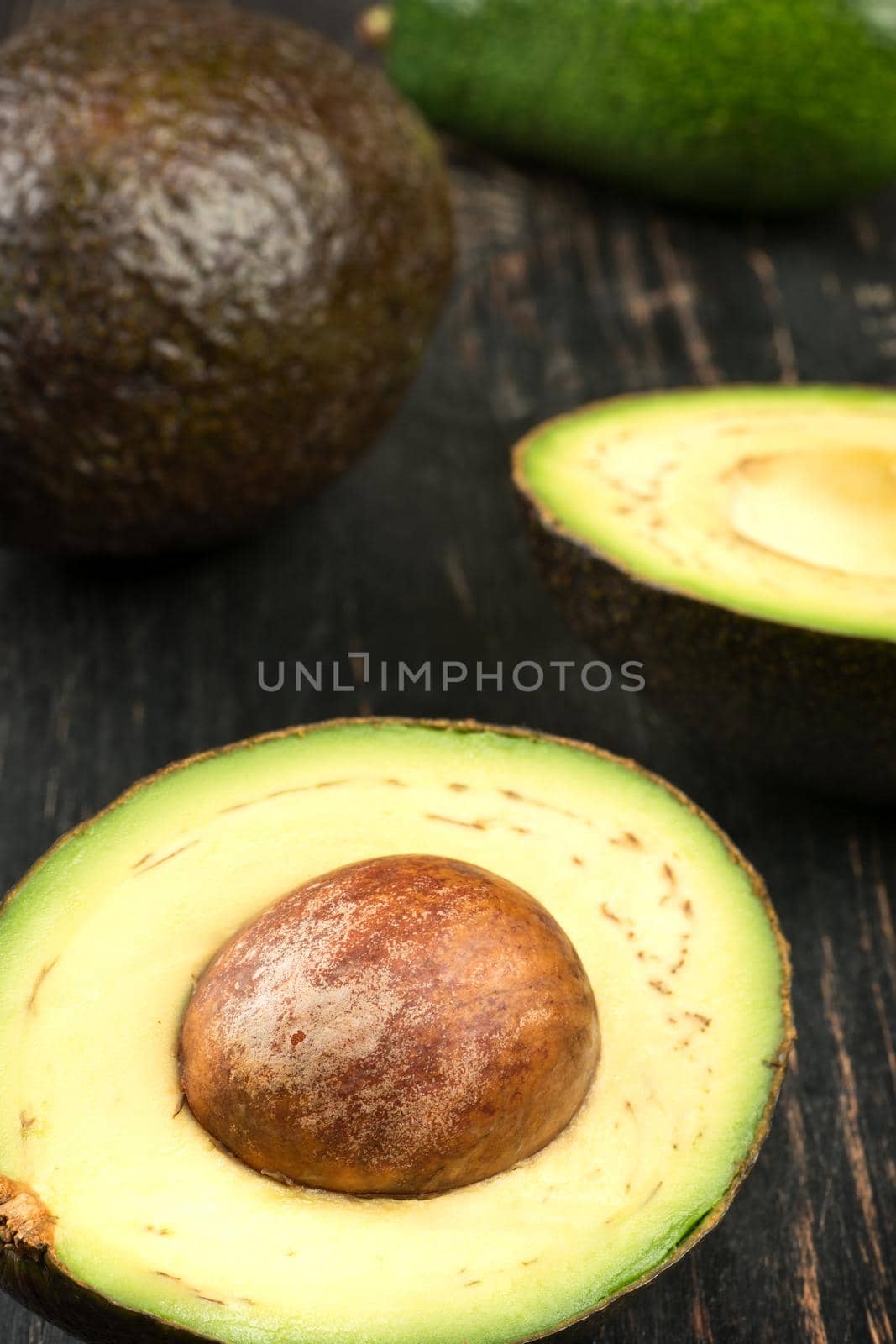Fresh Hass avocado with half on wooden background, closeup