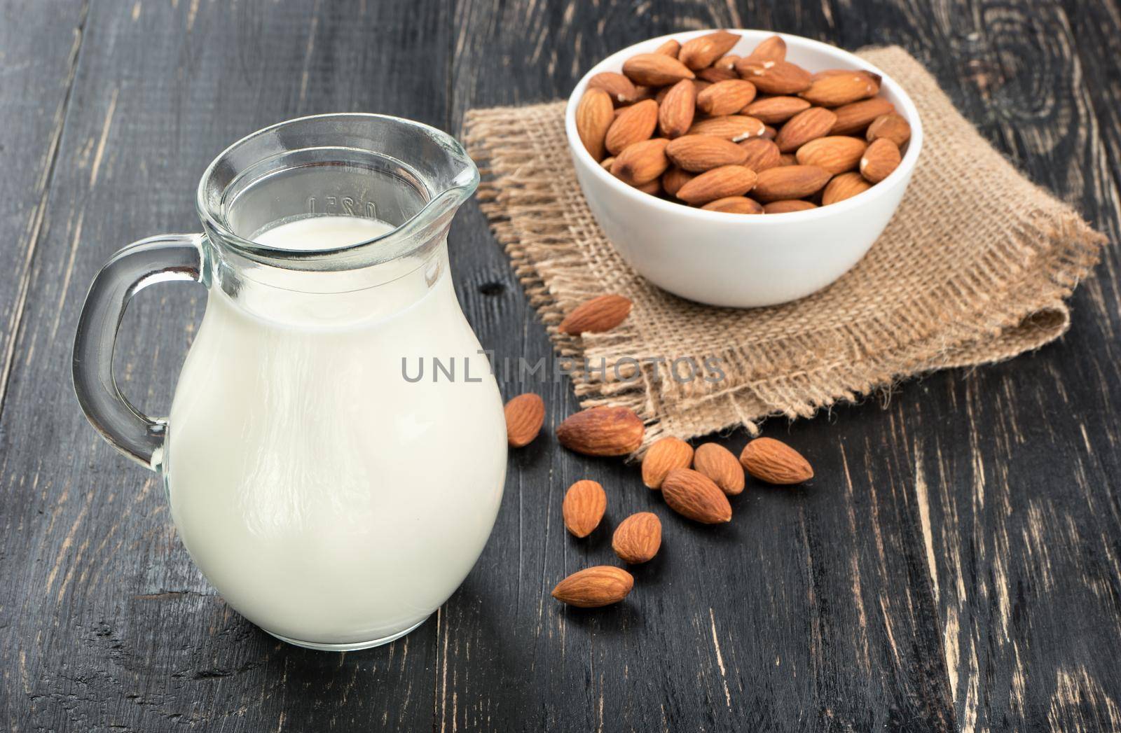 Bowl of nuts with a pitcher of almond milk on a dark table