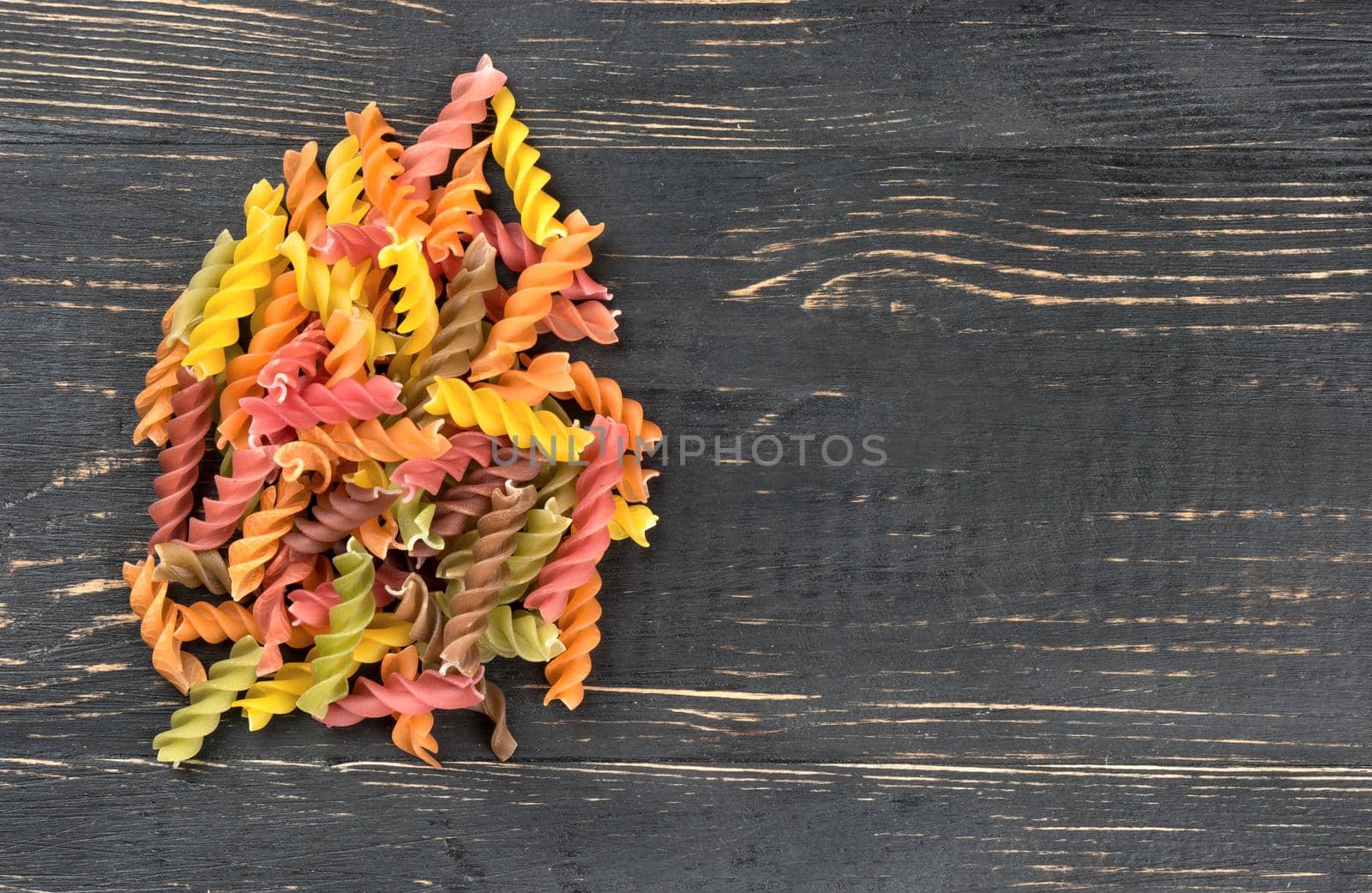 Scatter the colored pasta fusilli on an empty wooden background