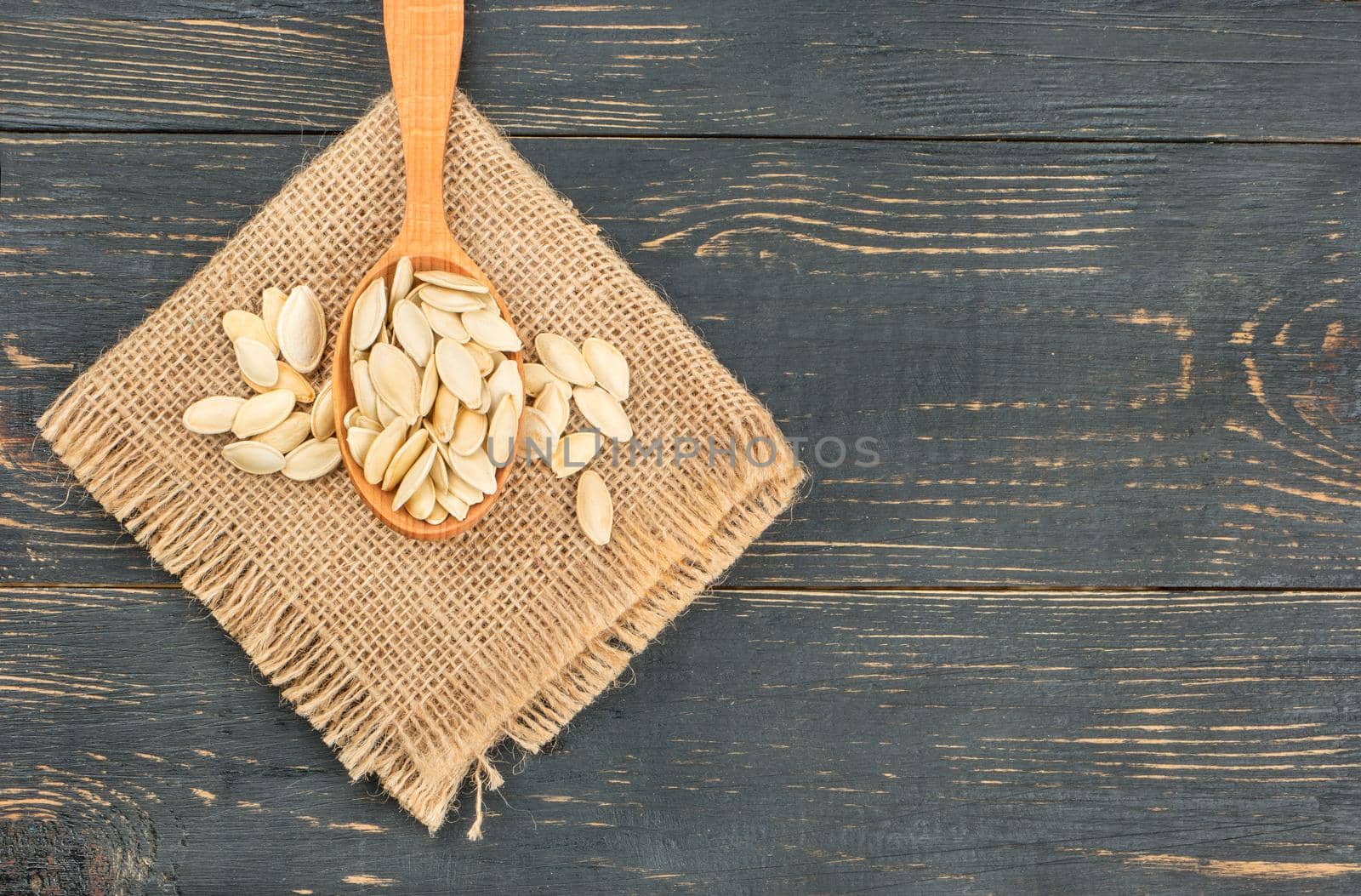 Pumpkin seeds in shell on burlap on wooden background closeup