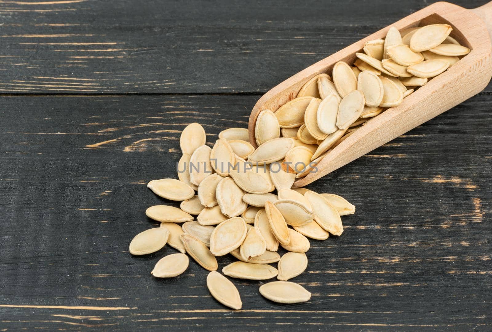 Pumpkin seeds in scoop on wooden background closeup