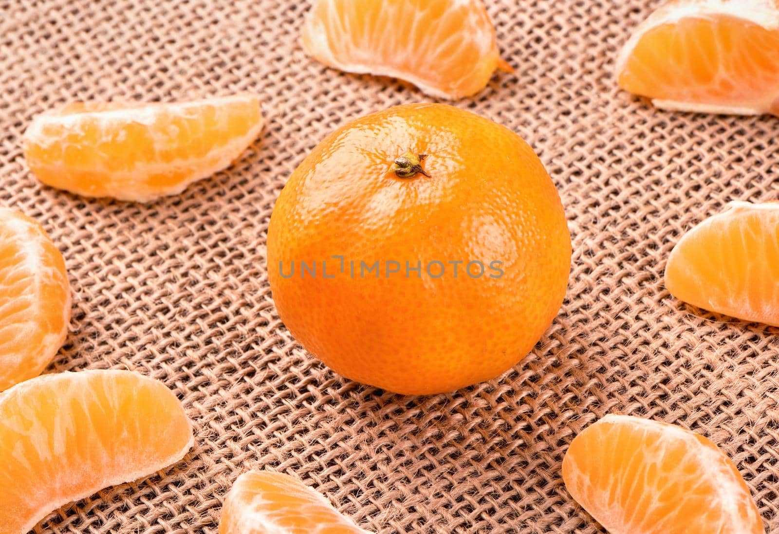 A ripe fruit mandarine with scattered  slices on sackcloth