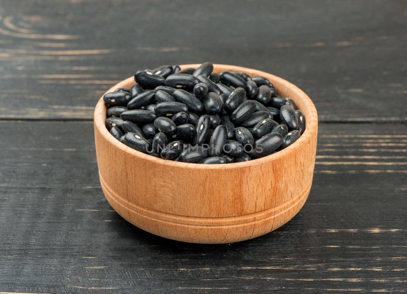 Small bowl with black beans on wooden background
