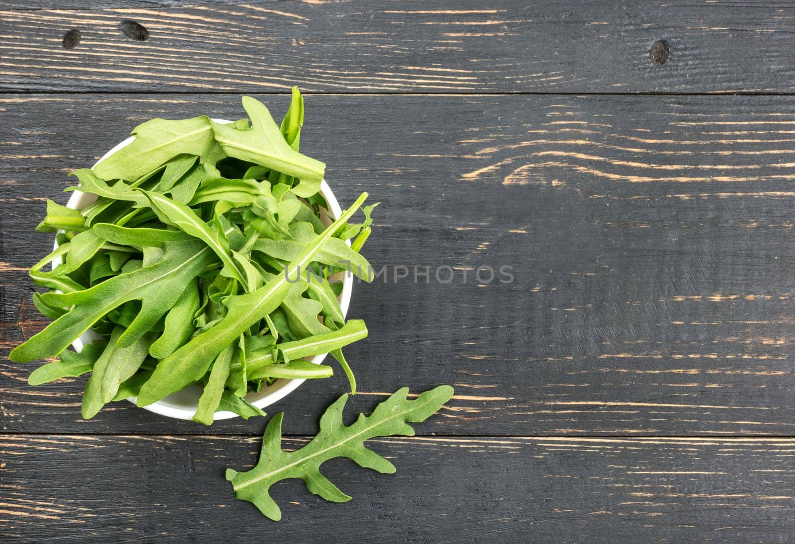 Ceramic bowl with fresh arugula on empty wooden background