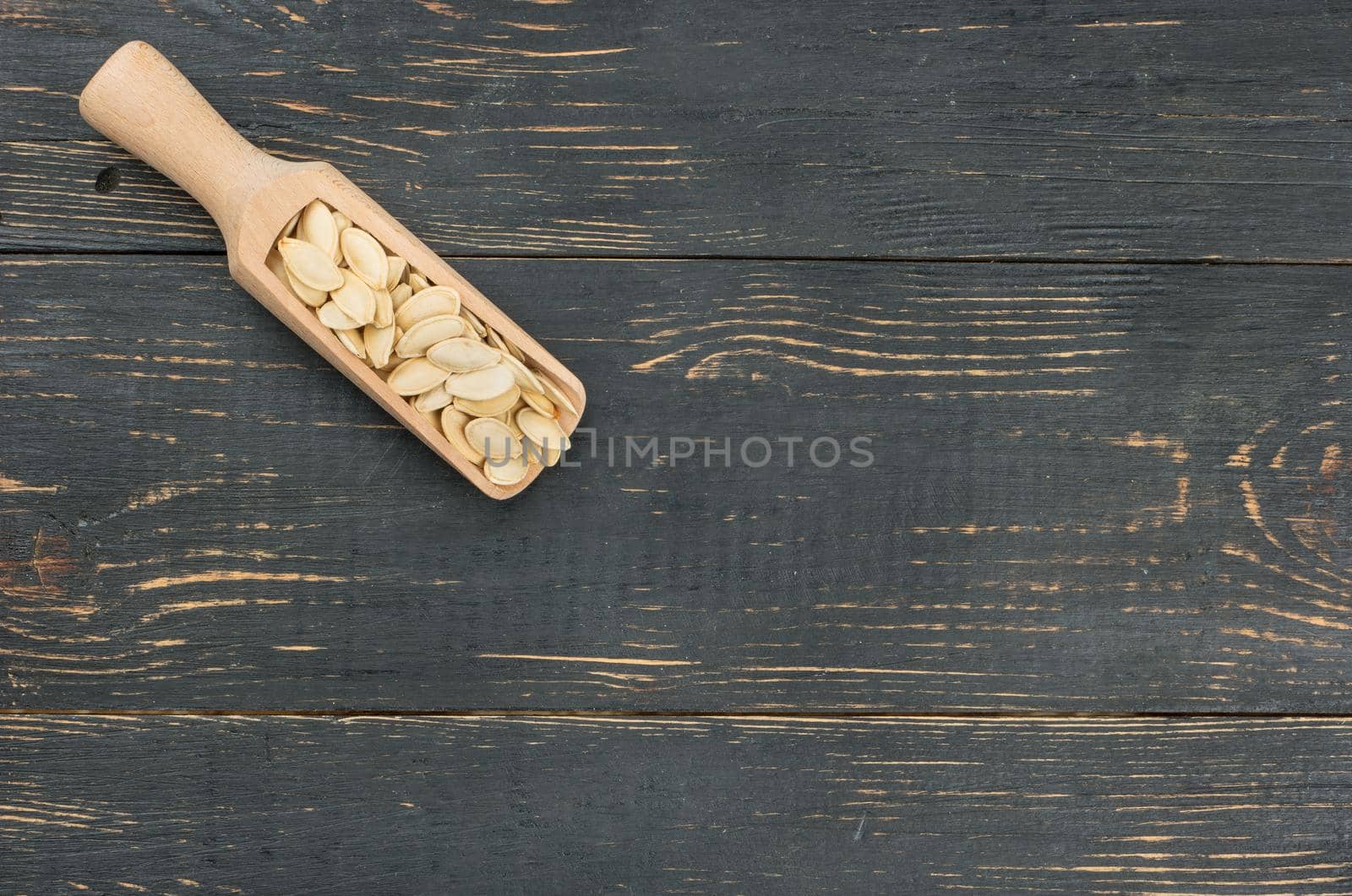 Pumpkin seeds in scoop on empty wooden background