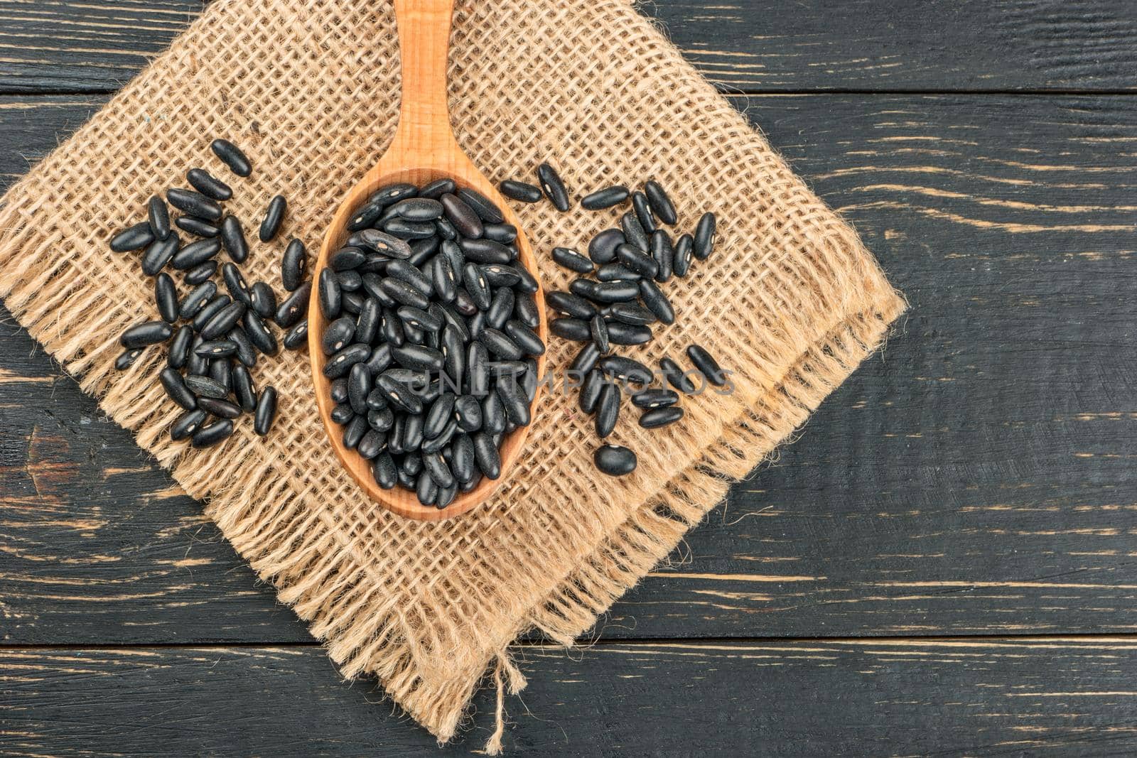 Black beans in wooden spoon on burlap and wooden background closeup
