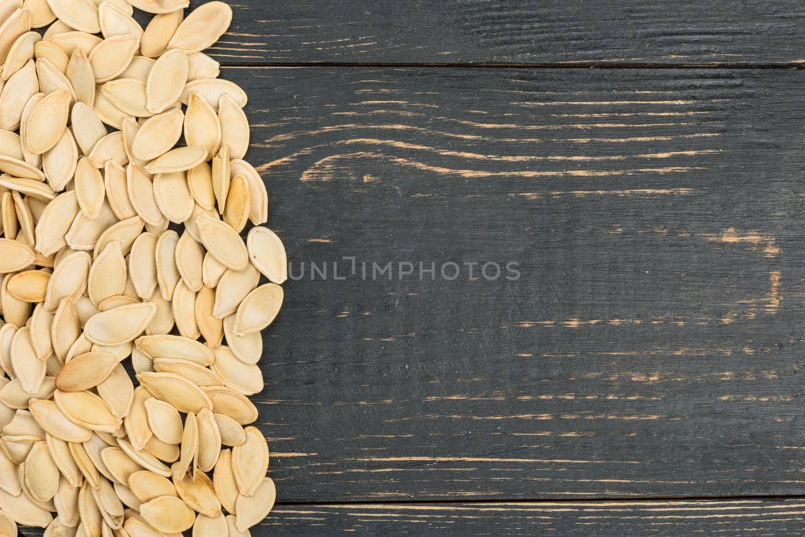 Scattered pumpkin seeds on an empty wooden background, top view