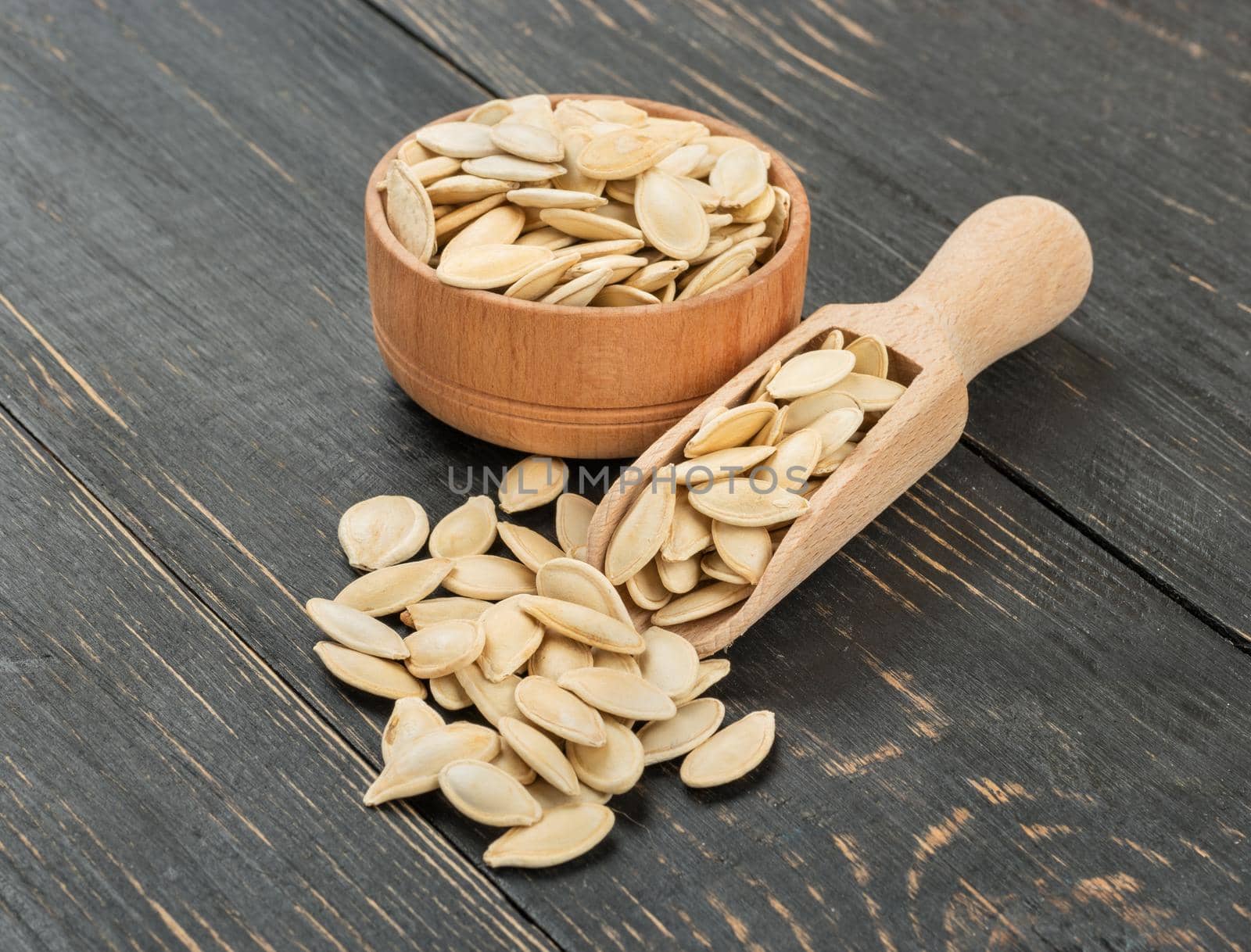 Pumpkin seeds in scoop and bowl on wooden background