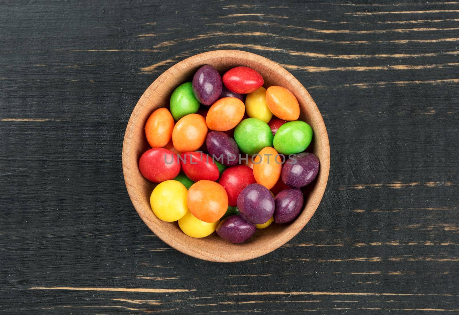 Multicolored candy in a bowl on a wooden background top view