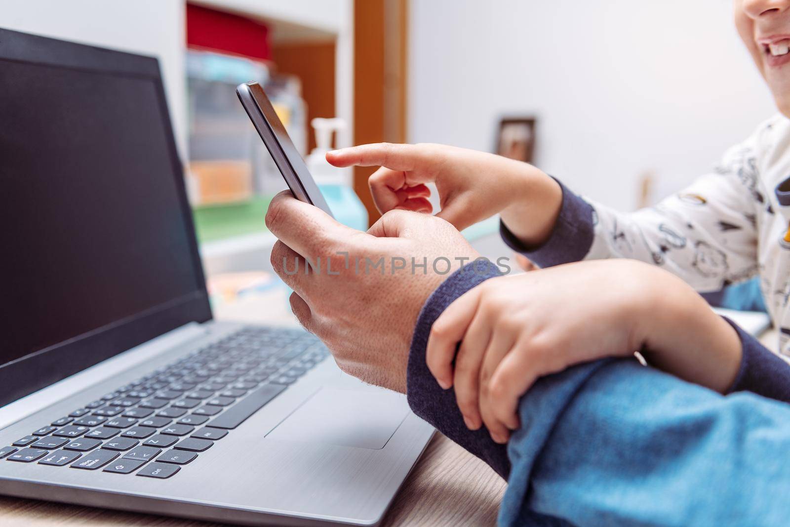 detail of a child hands bothering his father while working at home with his smartphone and computer, work at home concept due to the coronavirus pandemic