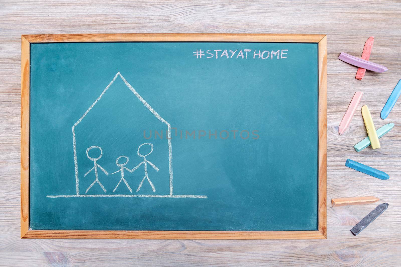 confined family drawn on a blackboard with the message stay at home and colored chalk next to it, concept of quarantine with children, copy space for text