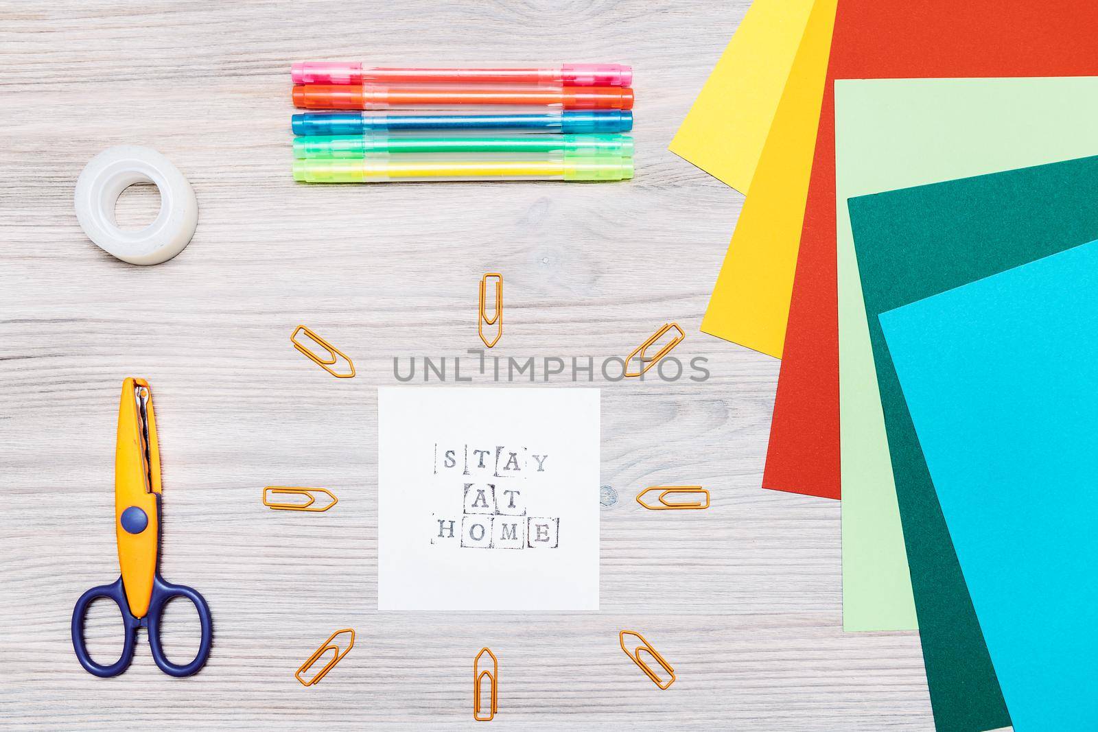 top view of material for making crafts on a wooden table and a paper with the message stay at home, copy space for text, concept of art and leisure for children in quarantine