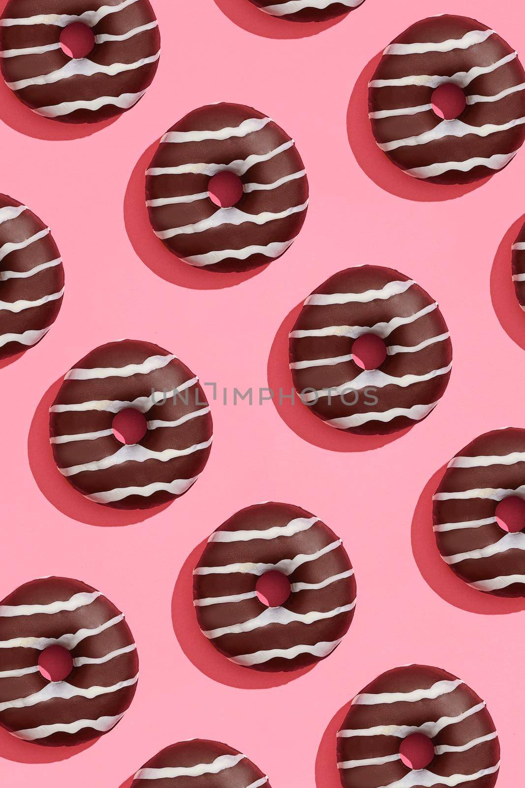 Concept food design with tasty chocolate glazed donut with white strips on coral pink pastel background top view pattern. Mock up, flat lay style