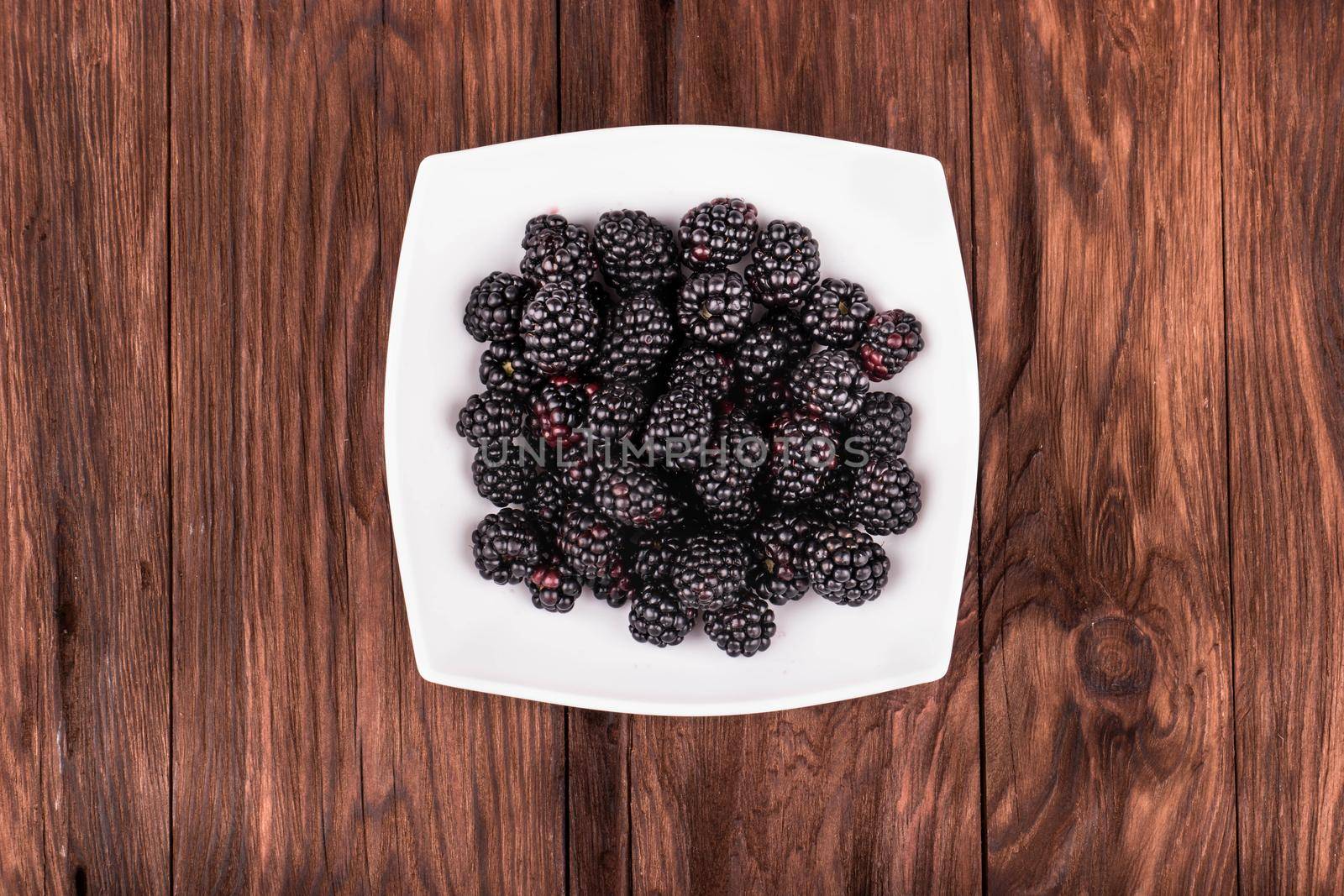White bowl filled with fresh blackberries on wooden background top view