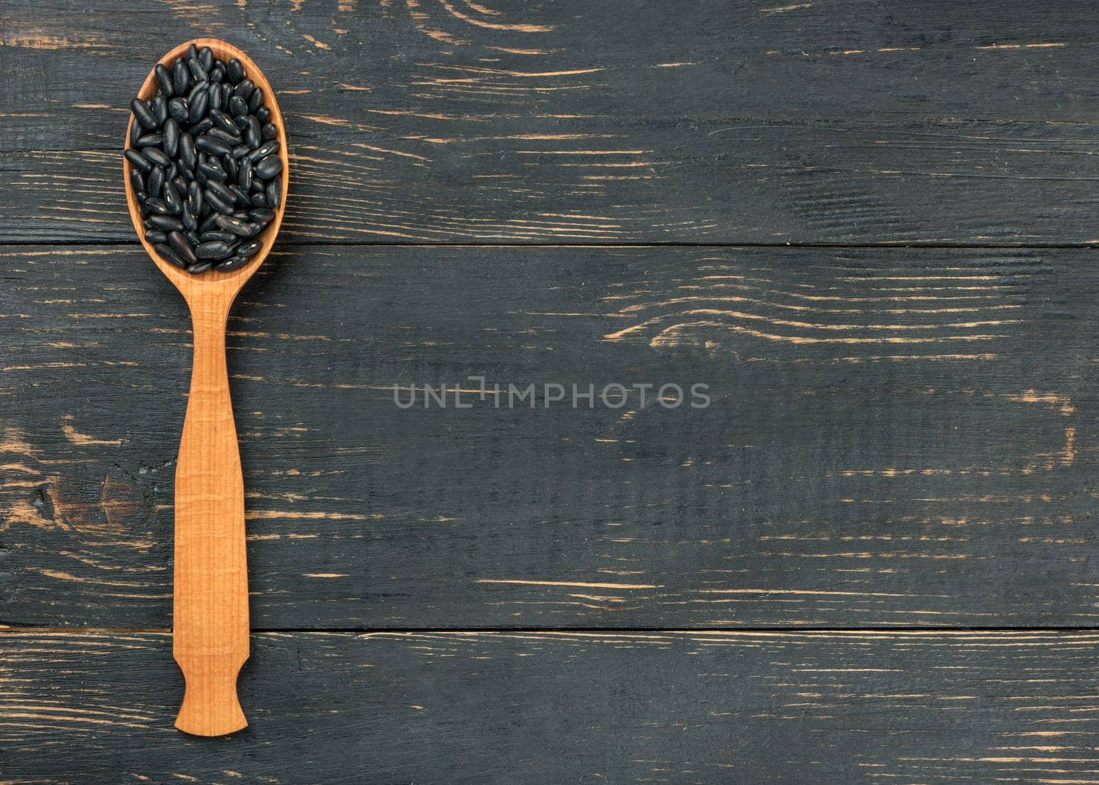Black beans in wooden spoon on empty wooden background